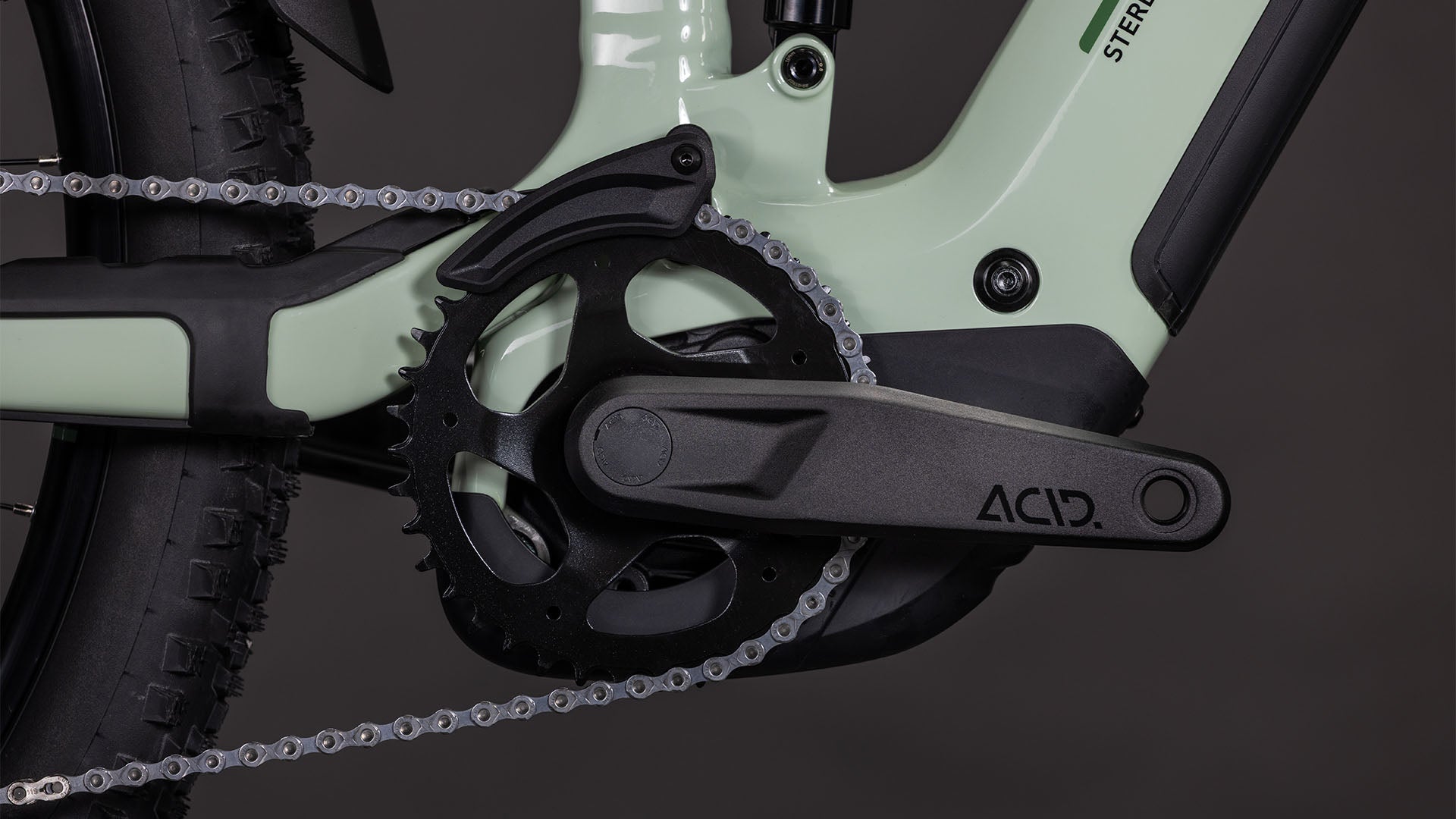 Nahaufnahme der schwarzen Kurbelgarnitur und des Kettenblatts an einem hellgrünen Cube Stereo Hybrid ONE22 Pro 800 stonegrey'n'black 2026, mit CUBE Schriftzug am Kurbelarm, E-Mountainbike-Reifen, Antrieb und Bosch CX Antriebssystem.