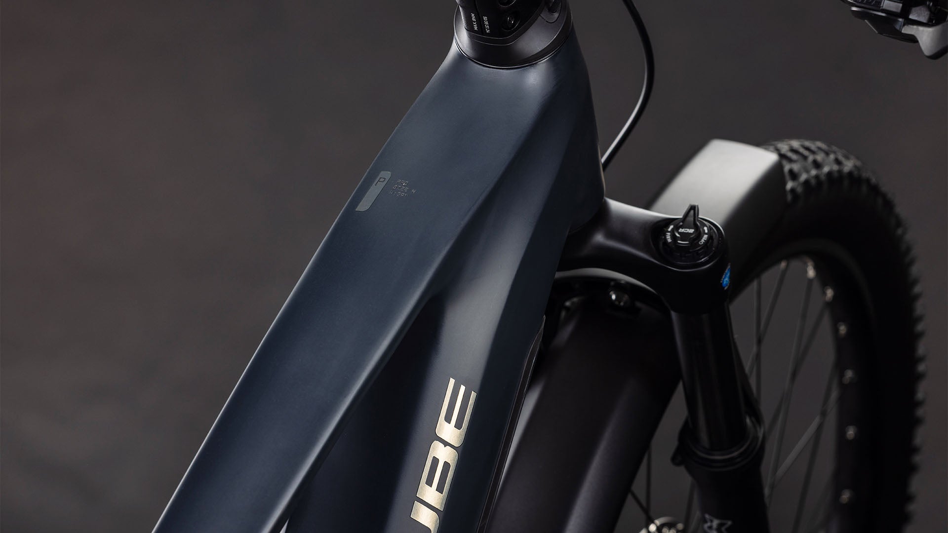 Nahaufnahme des Cube Stereo Hybrid ONE22 Pro 800 FE night'n'chrome 2026 E-Bikes von CUBE. Zu sehen sind das mattschwarze Oberrohr, die Vordergabel, der Bosch CX Motor, ein Teil des Lenkers und der Federung sowie das CUBE Logo auf dunklem Hintergrund.