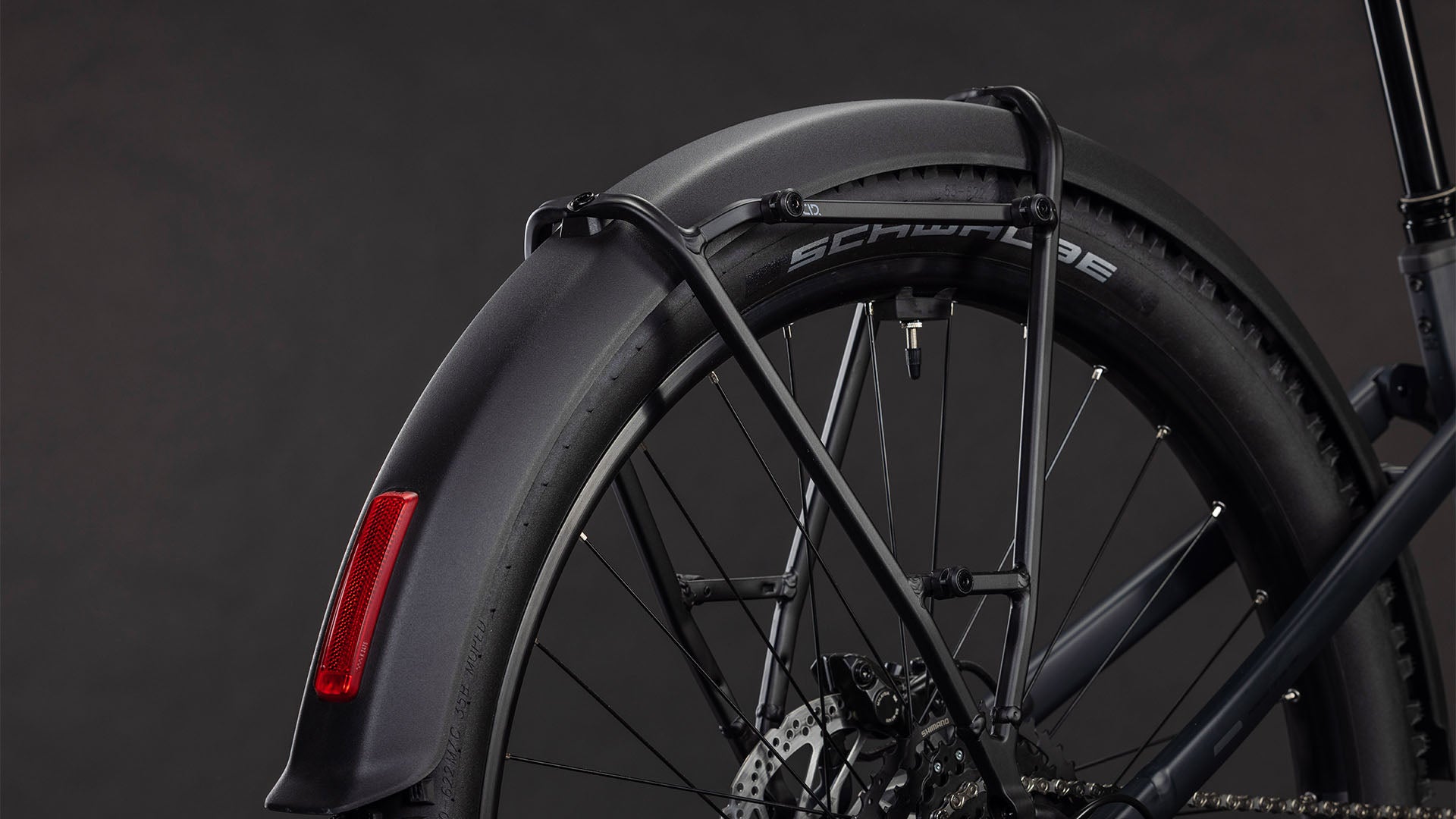 Nahaufnahme des Hinterrads des CUBE Stereo Hybrid ONE22 Pro 800 FE night'n'chrome 2026 mit schwarzem Schutzblech, Rückstrahler, Schwalbe-Reifen, Shimano Cues 10-fach Schaltung und detailliertem Bremssystem vor dunklem Hintergrund.
