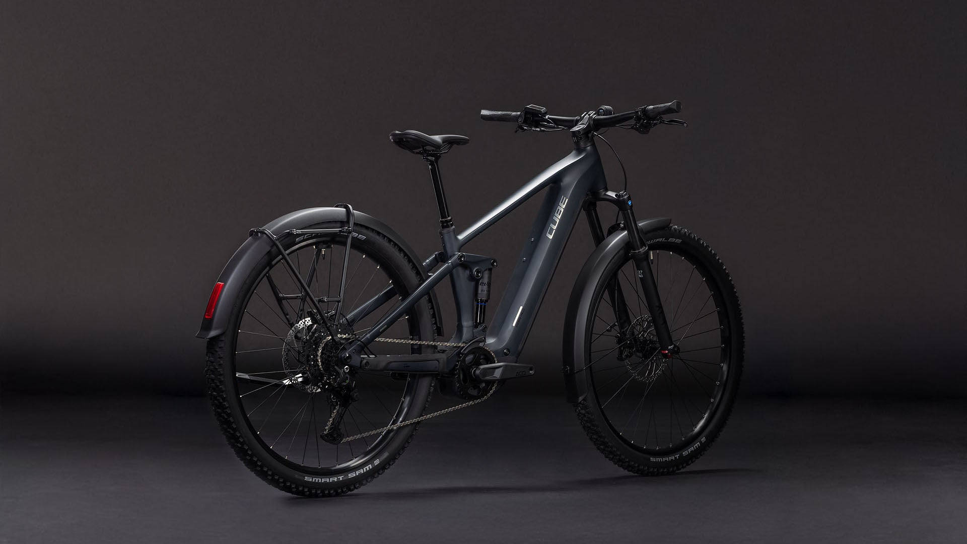 Das CUBE Stereo Hybrid ONE22 Pro 800 FE night'n'chrome 2026 verfügt über einen mattgrauen Rahmen, einen Bosch CX-Motor, eine Vorderradaufhängung, dicke Reifen, Scheibenbremsen und ein hinteres Schutzblech - und das alles vor einem dunklen Hintergrund.