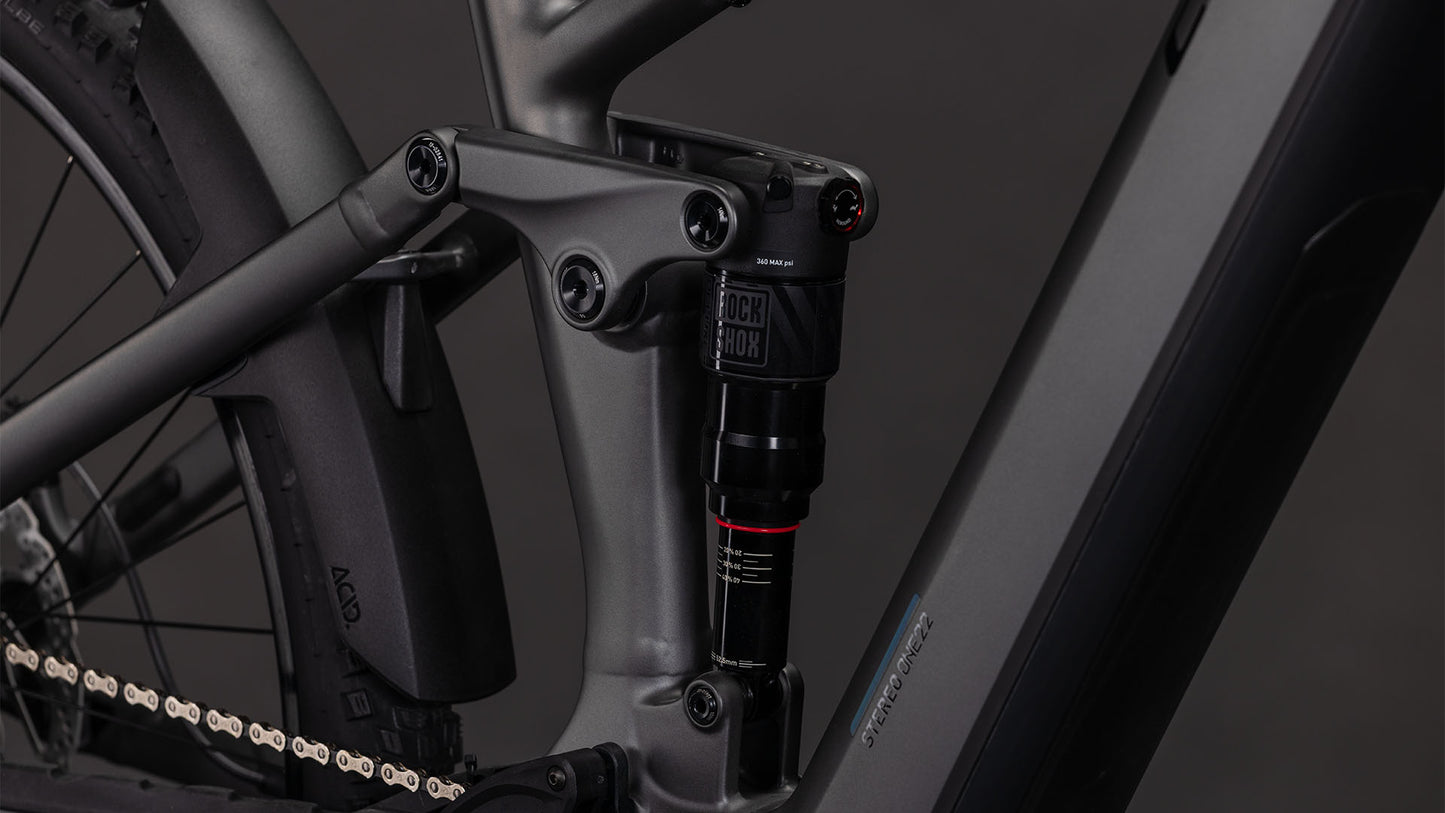 Nahaufnahme des CUBE Stereo Hybrid ONE22 Race 800 slabgrey'n'chrome 2026 von CUBE. Zu sehen sind die Hinterradfederung mit RockShox-Dämpfer, der Bosch CX-Motor, der sauber in den matten Rahmen integriert ist, sowie Kette und Hinterrad.
