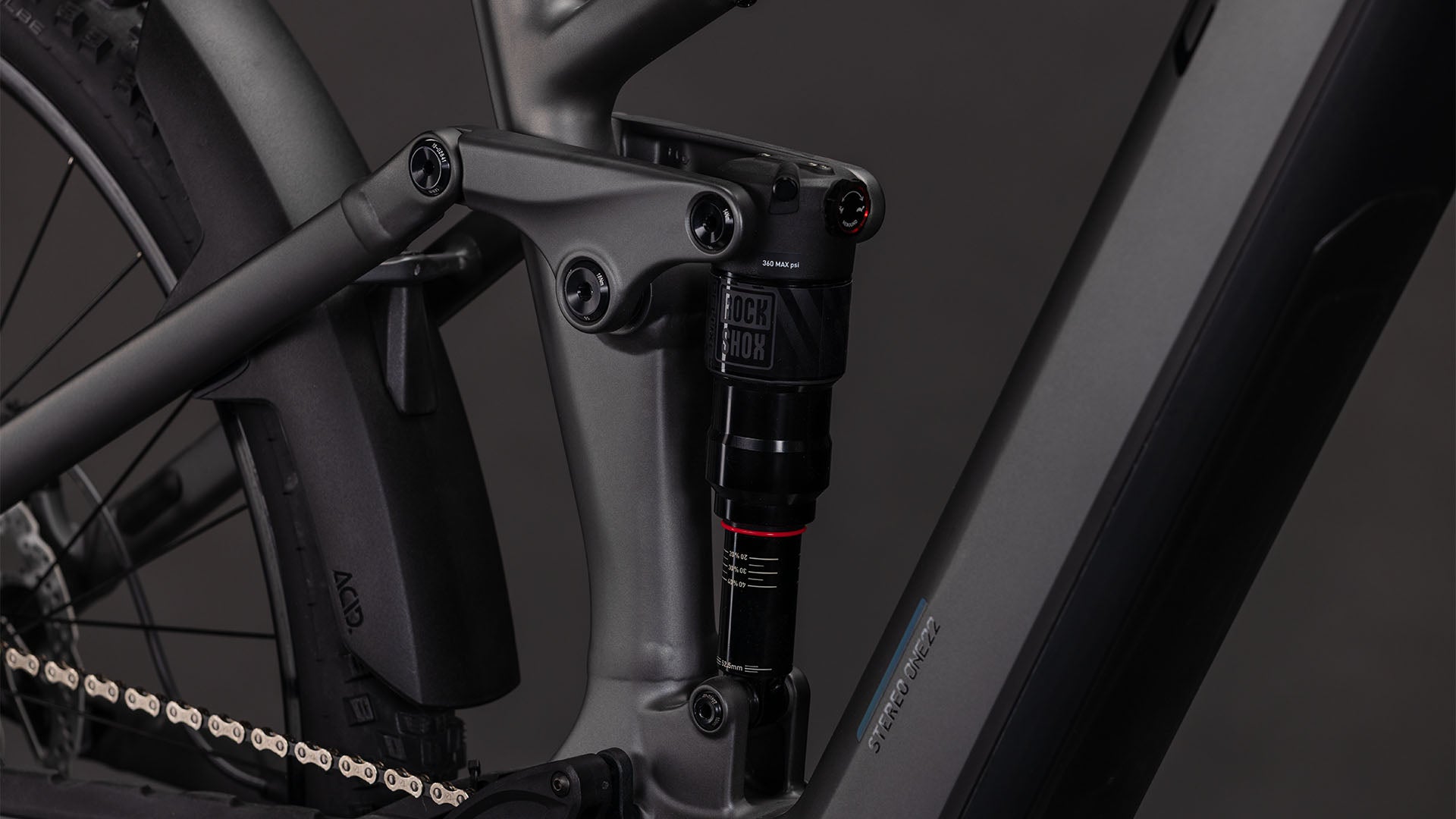 Nahaufnahme des CUBE Stereo Hybrid ONE22 Race 800 slabgrey'n'chrome 2026 von CUBE. Zu sehen sind die Hinterradfederung mit RockShox-Dämpfer, der Bosch CX-Motor, der sauber in den matten Rahmen integriert ist, sowie Kette und Hinterrad.