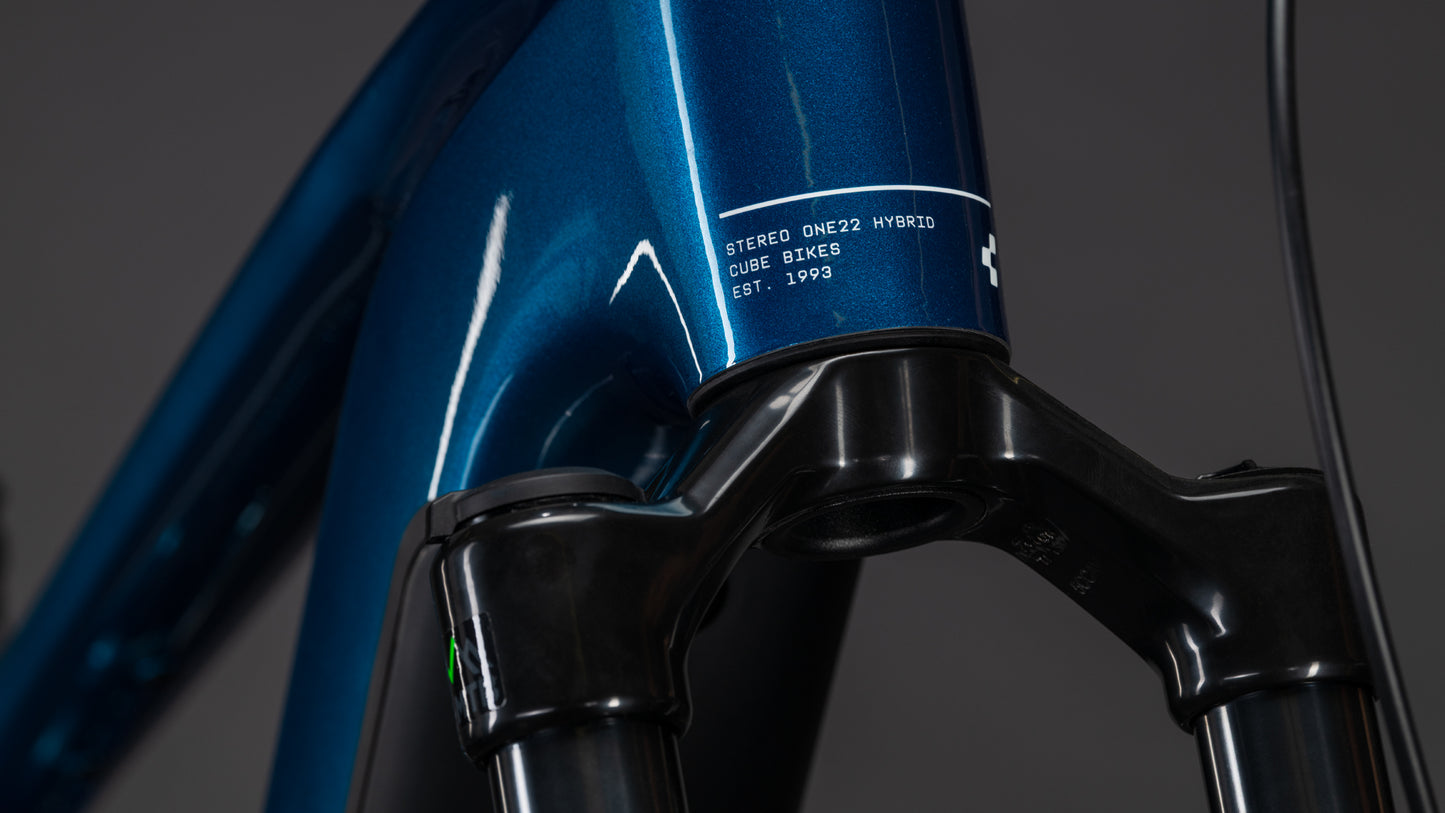Nahaufnahme eines blauen CUBE Stereo Hybrid ONE22 Race 800 electricblue'n'white 2026 Rahmens mit Bosch CX Motor, der die vordere Federgabel und den Steuersatz vor einem dunklen Hintergrund zeigt.