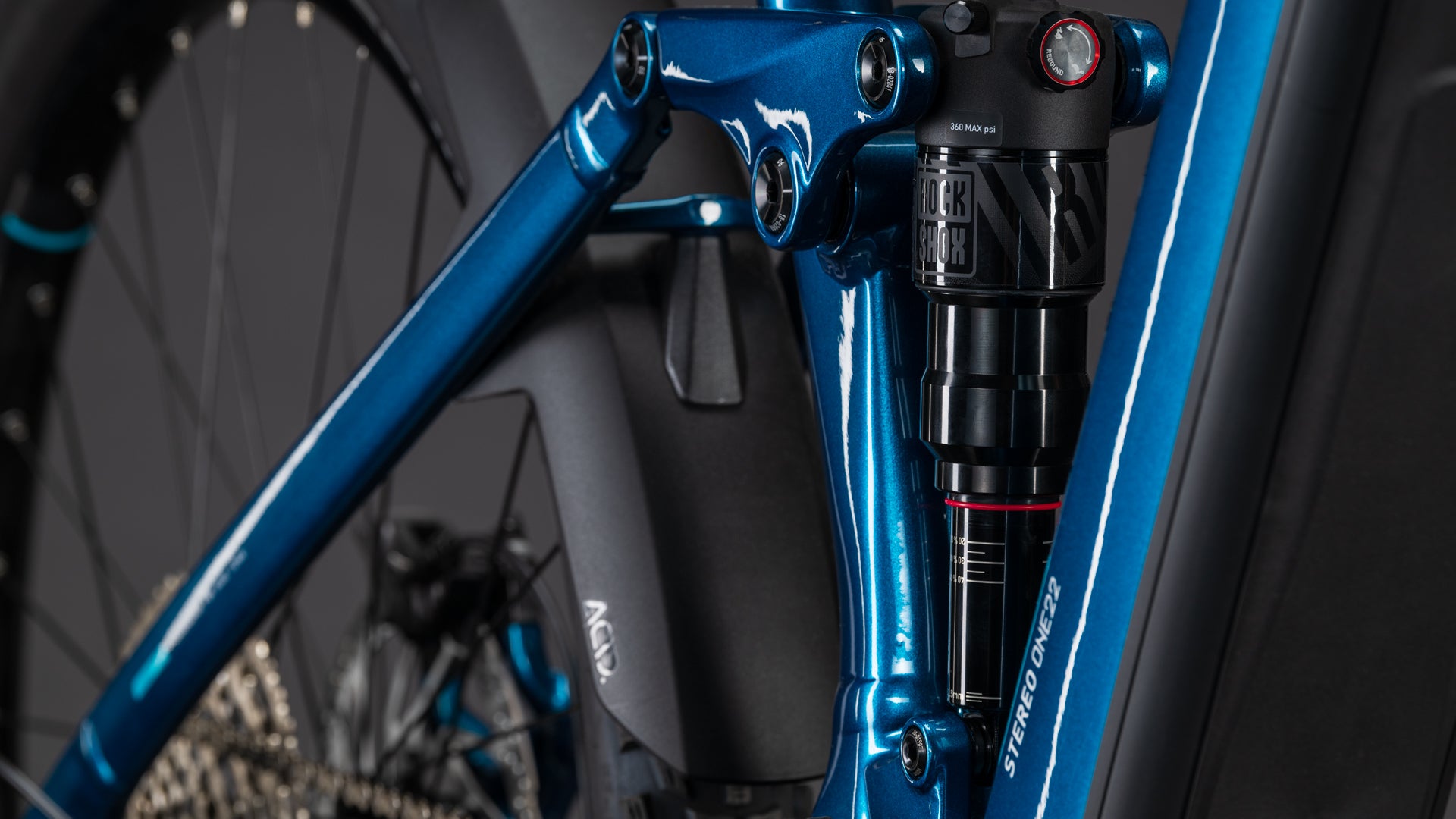 Nahaufnahme des CUBE Stereo Hybrid ONE22 Race 800 electricblue'n'white 2026 Rahmens, mit Hervorhebung der hinteren Federung und des Gestänges, wobei das Hinterrad, die Schaltung und die Shimano 12-fach XT-Kettenschaltung sichtbar sind.