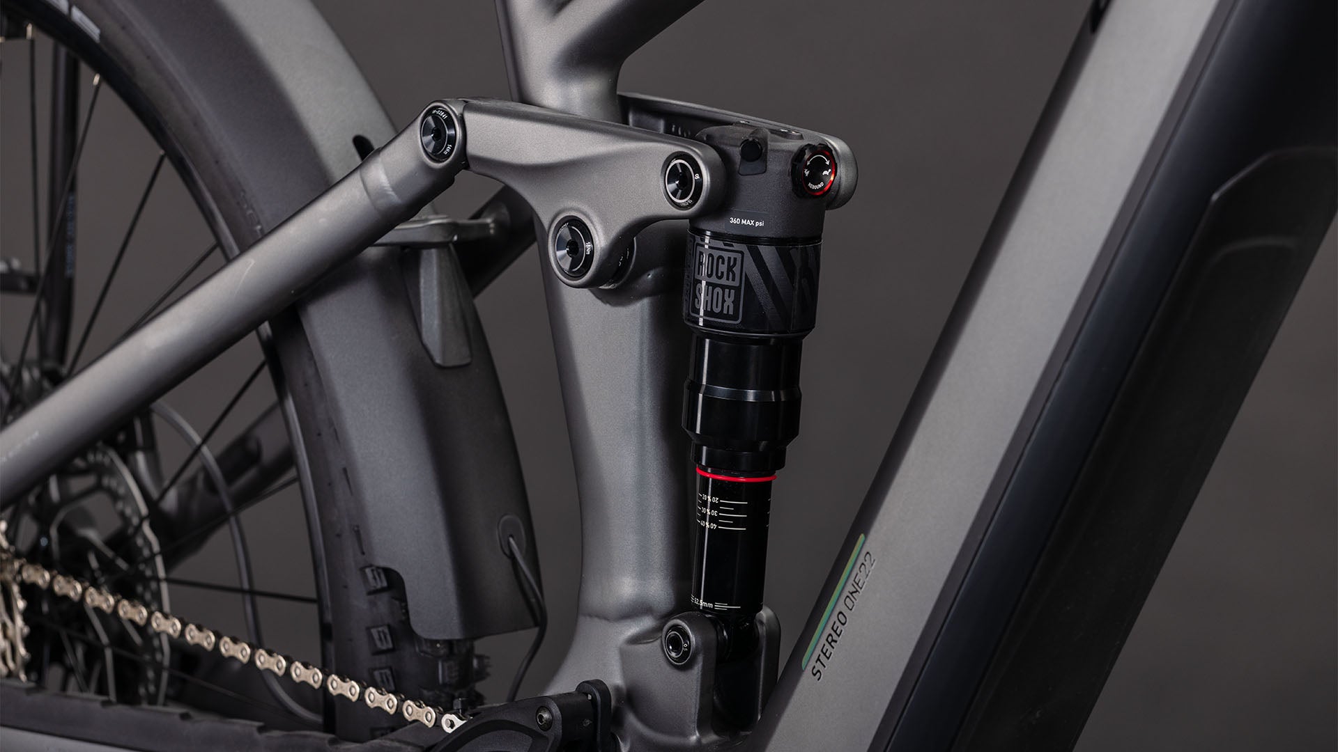 Nahaufnahme des CUBE Stereo Hybrid ONE22 Race 800 FE slabgrey'n'chrome 2026 Rahmens, die das mattgraue Finish, die Hinterradfederung mit RockShox Dämpfer und die sichtbare Kette in der Nähe des Hinterrads zeigt.