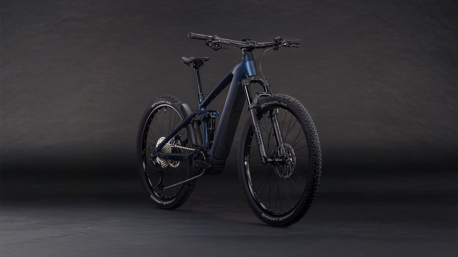 Das CUBE Stereo Hybrid ONE22 SLX 800 indigoblue'n'blue 2026, ein schnittiges E-MTB mit robuster Bereifung und Bosch CX-Antrieb, wird auf einem dunklen, nahtlosen Hintergrund gezeigt, der sein Front- und Seitenprofil hervorhebt.