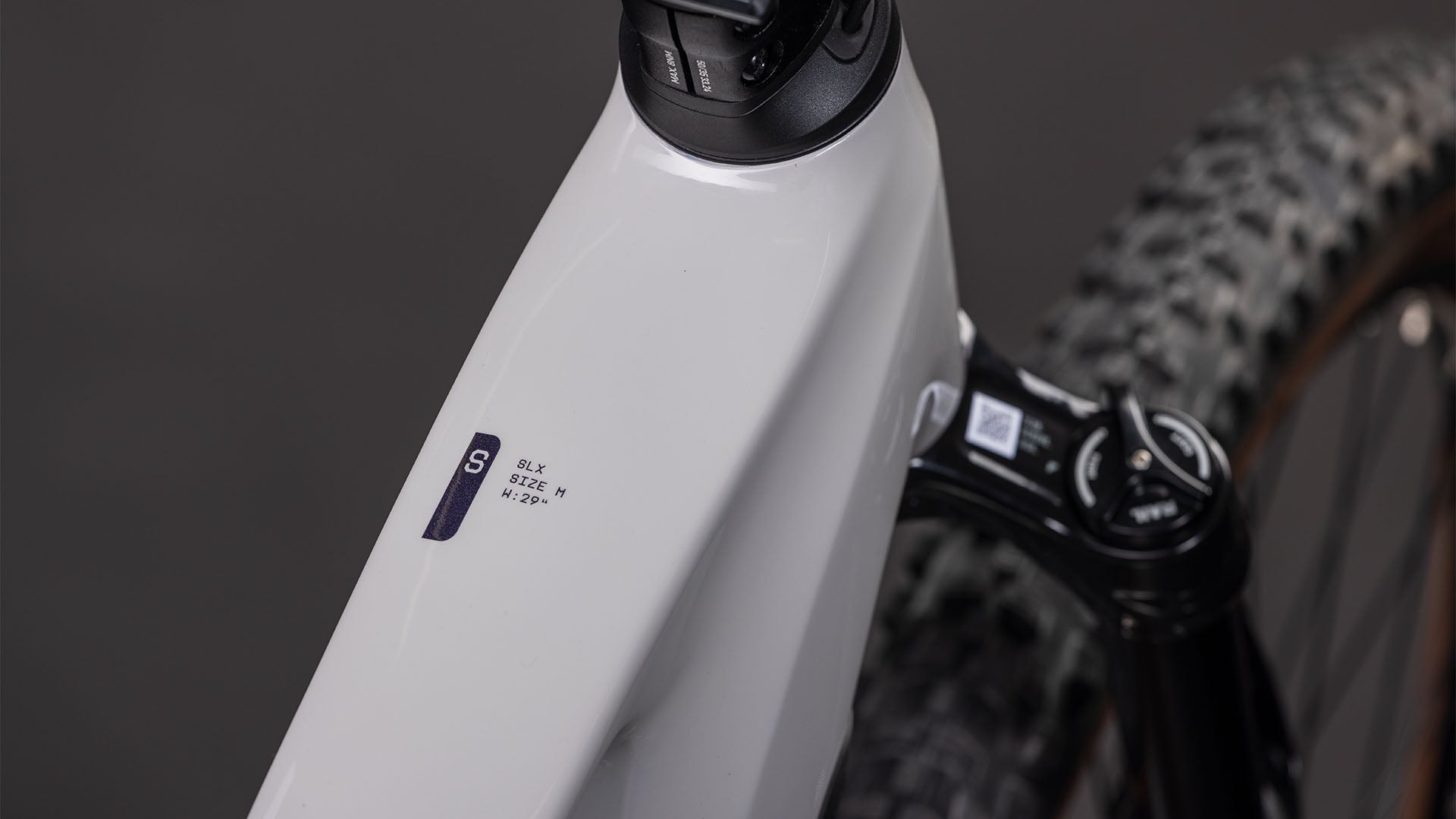 Nahaufnahme eines CUBE Stereo Hybrid ONE22 SLX 800 greige'n'switch 2026 Rahmens mit "SLX SIZE M M/17-18" Aufkleber, Federgabel, Knobby Reifen und Bosch CX Antrieb im Hintergrund.