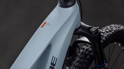 Nahaufnahme des mattgrauen Rahmens eines CUBE Stereo Hybrid ONE44 Pro 800 vulcan'n'orange 2026 Mountainbikes mit Federgabel, Noppenreifen und orangefarbenem Oberrohrschild; der Hintergrund ist dunkel und unscharf.