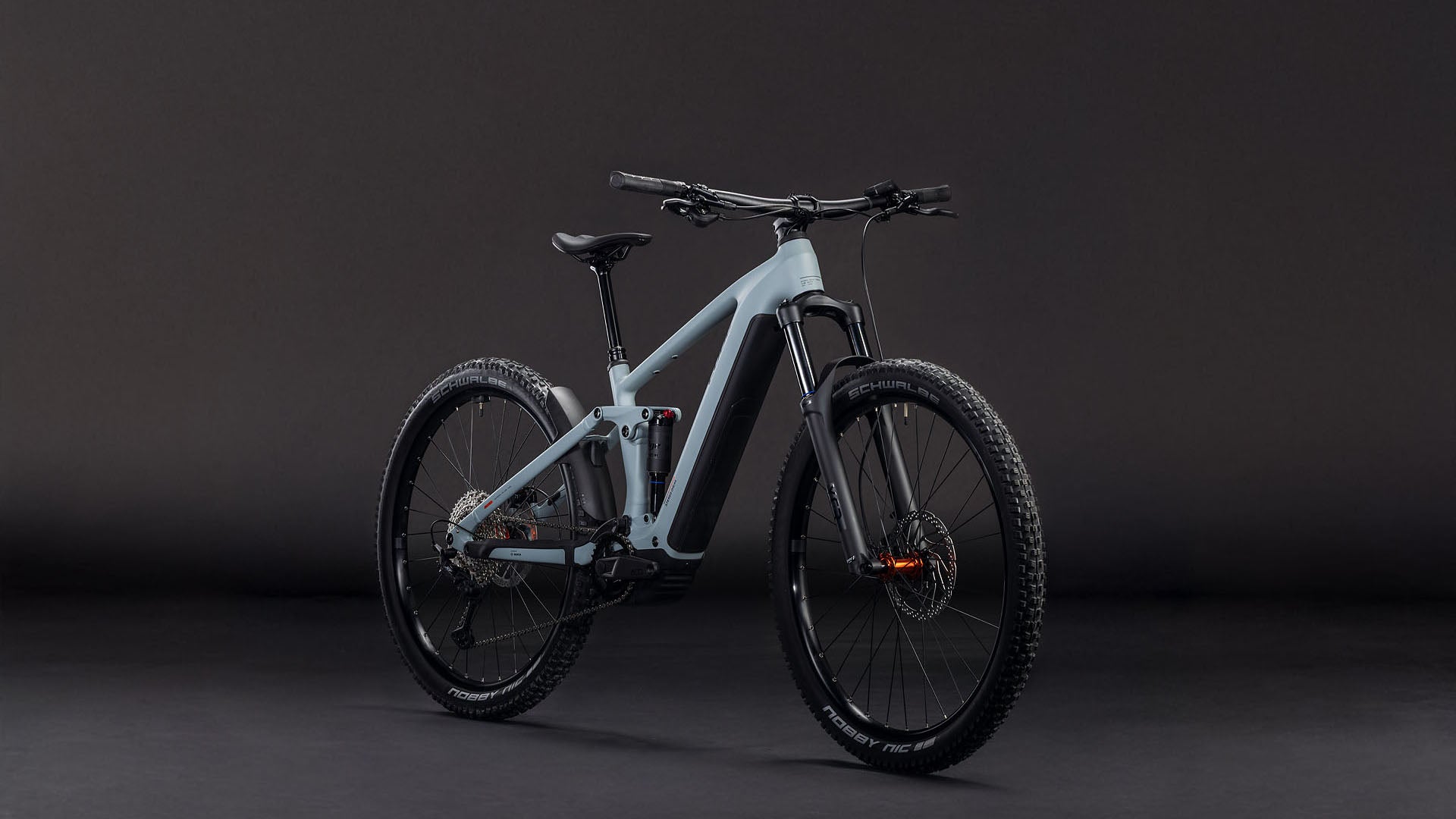 Das CUBE Stereo Hybrid ONE44 Pro 800 vulcan'n'orange 2026 Mountainbike mit dicken Reifen, Vorderradaufhängung und Shimano XT Schaltung ist vor einem dunklen Hintergrund abgebildet, der so angewinkelt ist, dass die Front und die linke Seite zu sehen sind.