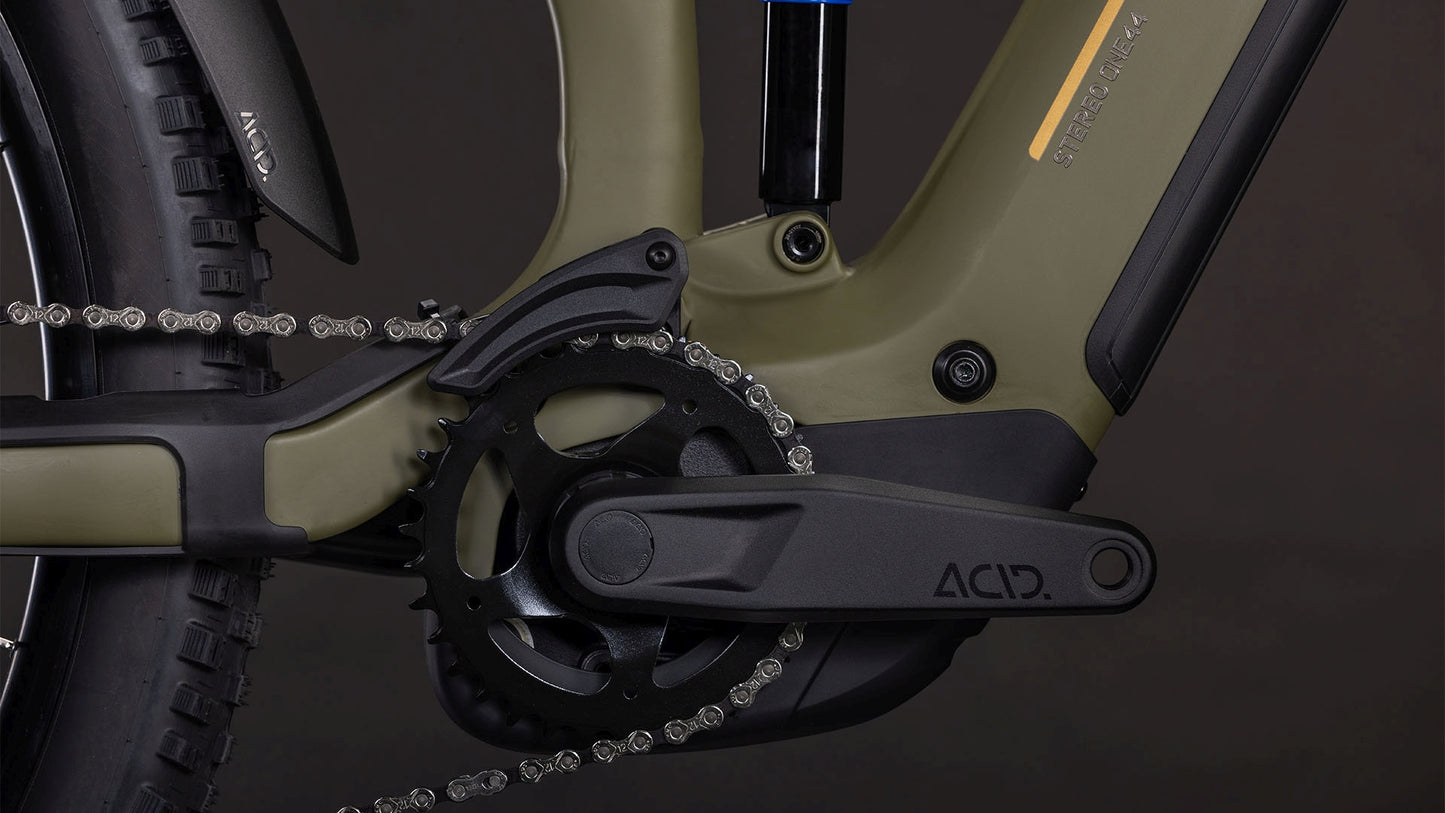 Nahaufnahme der Kurbelgarnitur und des Antriebs des CUBE Stereo Hybrid ONE44 Pro 800 dustyolive'n'gold 2026 mit Bosch CX Motor, Shimano XT Schaltung, Kette, Pedalen und mattem olivgrünem und schwarzem Rahmen vor dunklem Hintergrund.