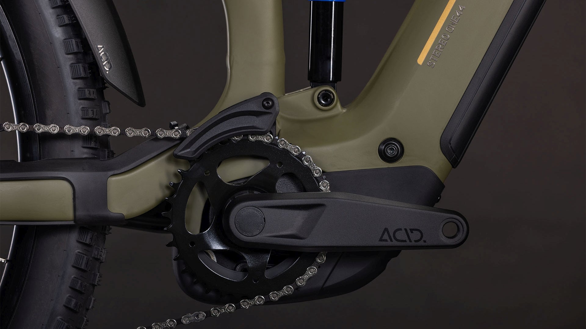 Nahaufnahme der Kurbelgarnitur und des Antriebs des CUBE Stereo Hybrid ONE44 Pro 800 dustyolive'n'gold 2026 mit Bosch CX Motor, Shimano XT Schaltung, Kette, Pedalen und mattem olivgrünem und schwarzem Rahmen vor dunklem Hintergrund.