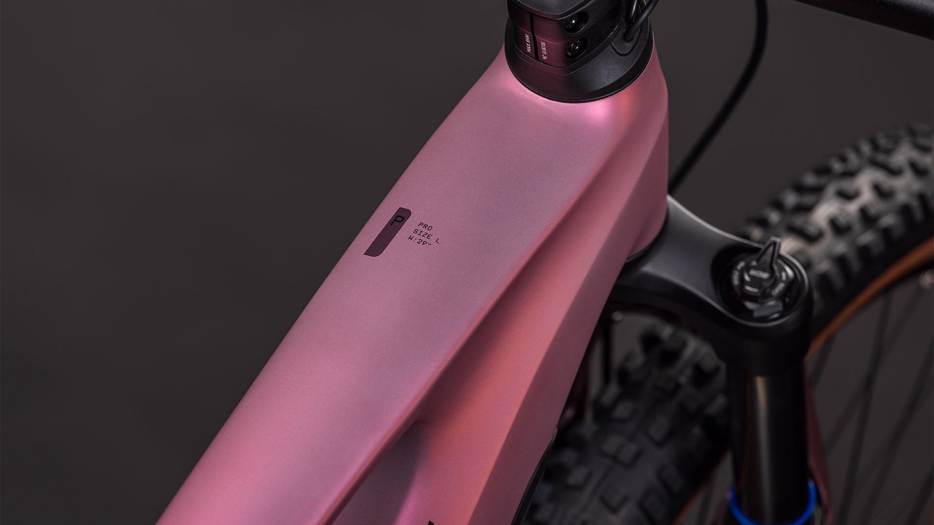 Nahaufnahme des CUBE Stereo Hybrid ONE44 Pro 800 shiftblush'n'raisin 2026 Rahmens, die das Oberrohr, die Federgabel und ein kleines Display zeigt. Ausgestattet mit Bosch CX-Motor; der Hintergrund ist dunkel und unscharf.