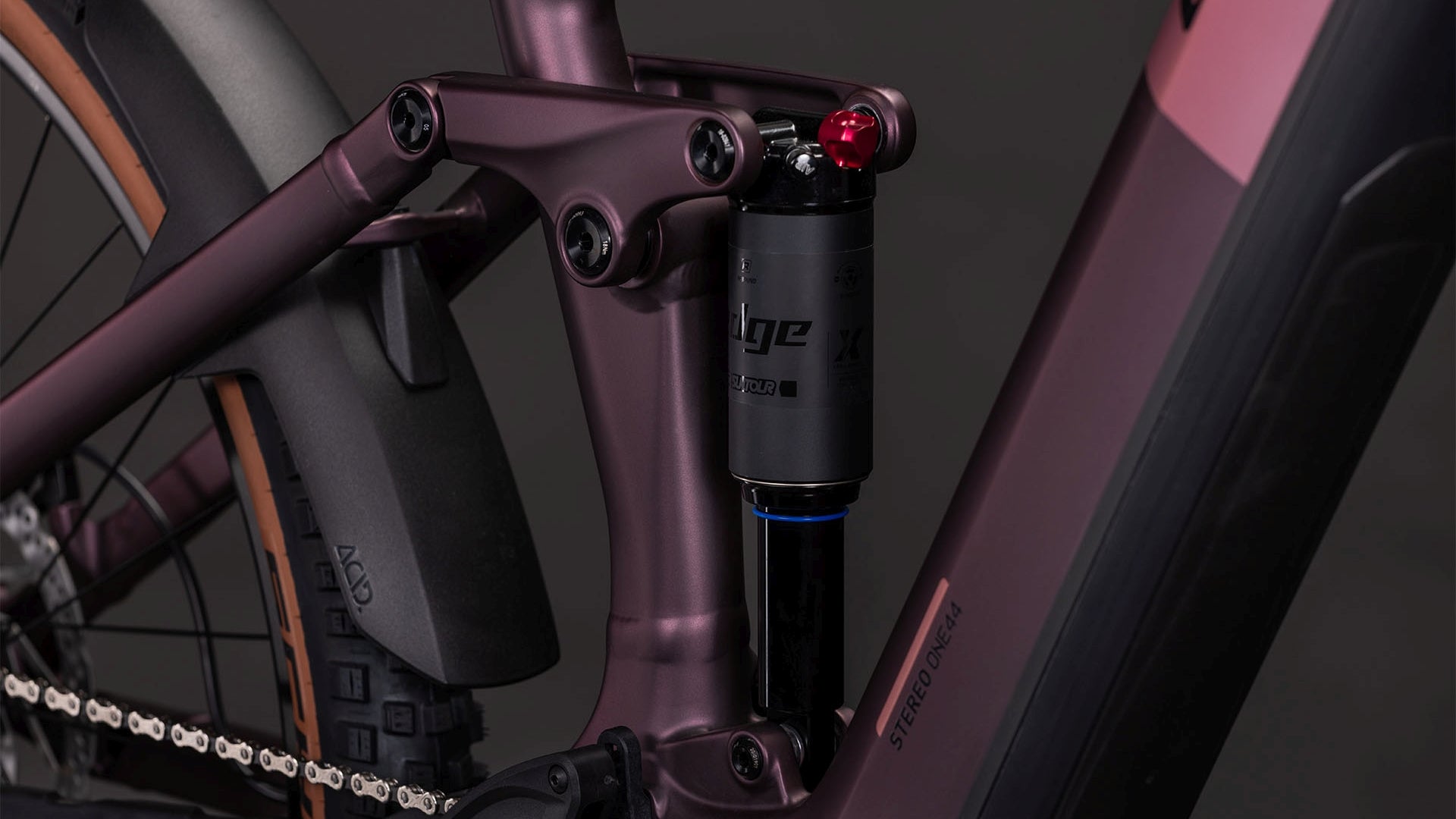 Nahaufnahme eines CUBE Stereo Hybrid ONE44 Pro 800 shiftblush'n'raisin 2026 mit schwarzem Stoßdämpfer am mattlila Rahmen mit Bosch CX Motor sowie Hinterrad, Kette und Schutzblech.