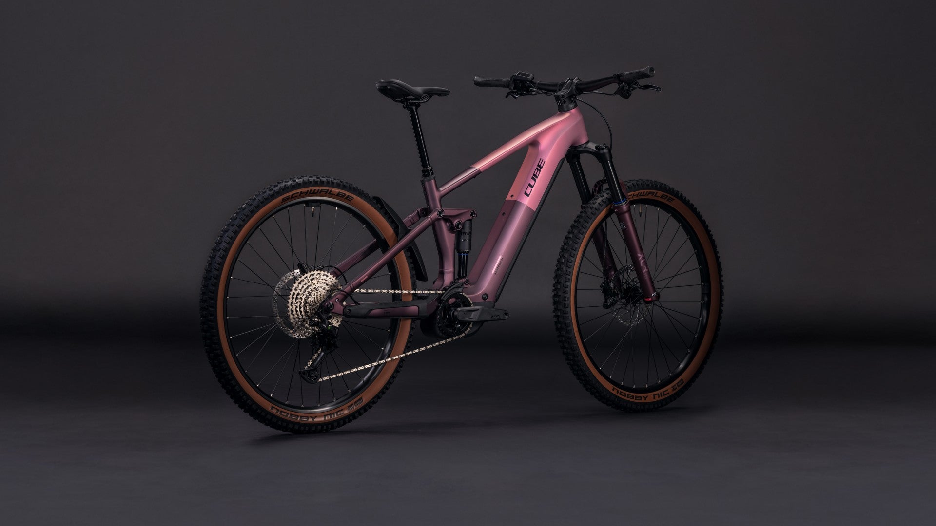 Das CUBE Stereo Hybrid ONE44 Pro 800 shiftblush'n'raisin 2026 Mountainbike mit mattrosa Lackierung, Shimano XT Schaltung, Federgabel und dicken Stollenreifen steht auf einem dunklen, nahtlosen Hintergrund.