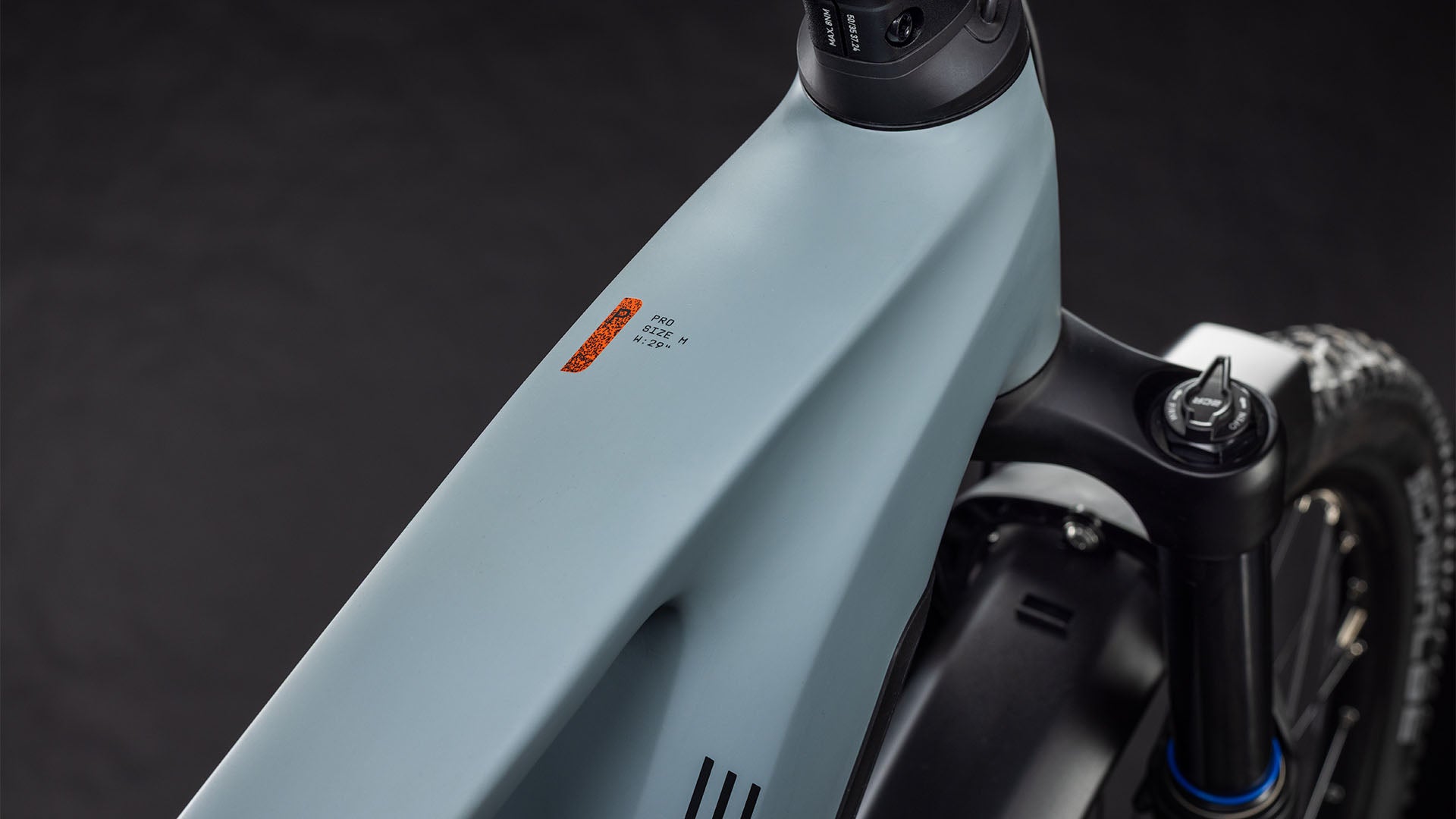 Nahaufnahme des Oberrohrs und der Vordergabel des CUBE Stereo Hybrid ONE44 Pro 800 FE vulcan'n'orange 2026, die den schlanken, mattgrauen Rahmen, das kleine orangefarbene Logo und den fortschrittlichen Bosch CX-Motor vor einem dunklen Hintergrund hervorhebt.