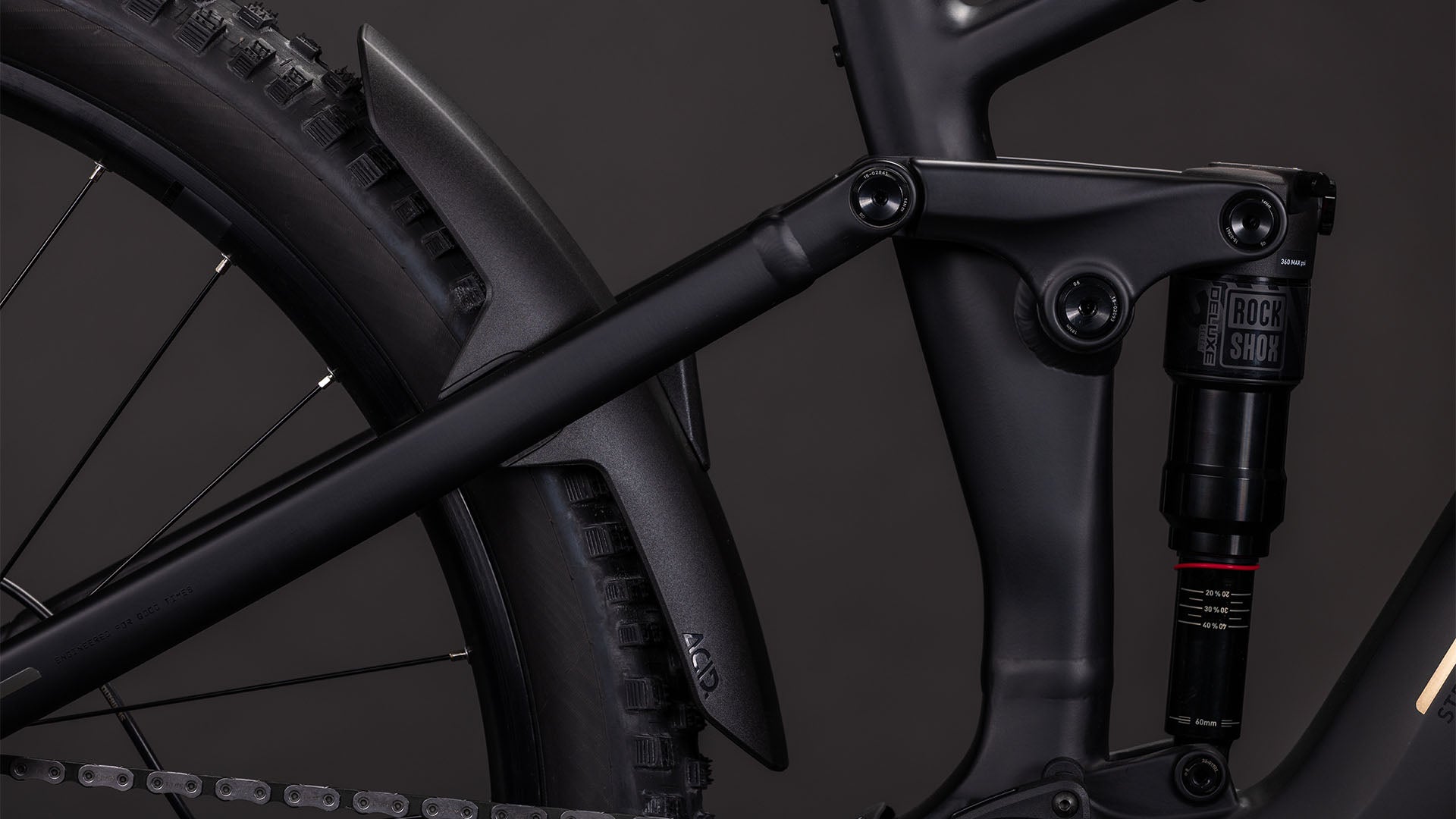 Die Nahaufnahme des CUBE Stereo Hybrid ONE44 EX 800 blackline 2026 zeigt den mattschwarzen Rahmen, die Hinterradfederung mit RockShox-Dämpfer, den Bosch CX-Antrieb und das Schutzblech oberhalb des Rades.
