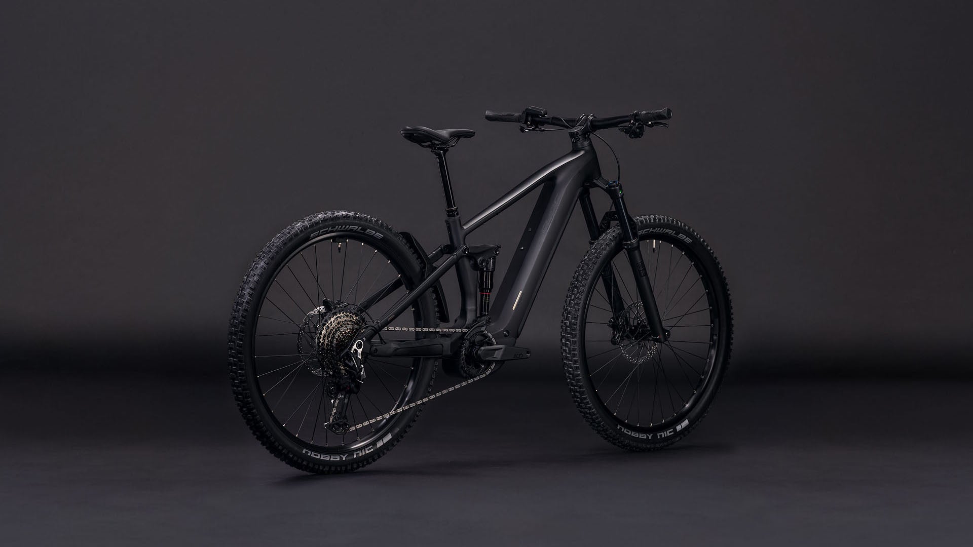 Das CUBE Stereo Hybrid ONE44 EX 800 blackline 2026 E-Bike ist schräg vor einem dunklen Hintergrund abgebildet. Die dicken Reifen und die Vollfederung unterstreichen sein modernes, mattschwarzes und robustes Design.