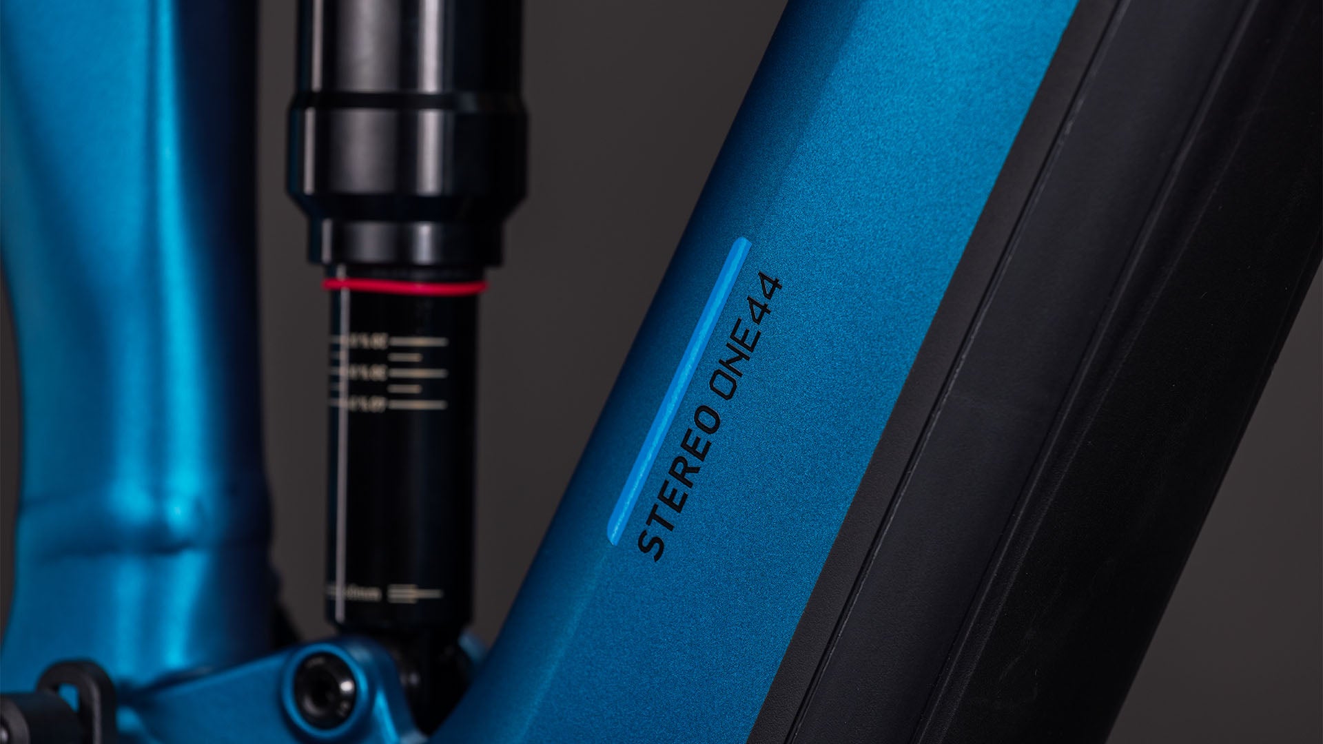 Nahaufnahme des CUBE Stereo Hybrid ONE44 EX 800 electricblue'n'blue 2026-Rahmens mit dem STEREO ONE44-Schriftzug, einem Teil des Aufhängungssystems, und mattschwarzen Akzenten vor dunklem Hintergrund.