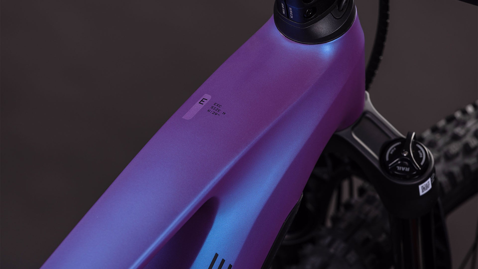 Nahaufnahme des CUBE Stereo Hybrid ONE44 EXC 800 blueiris'n'black 2026 Rahmens, wobei die lila-blaue Farbverlaufslackierung, die Federgabel und das Oberrohretikett vor einem dunklen, verschwommenen Hintergrund hervorgehoben werden.