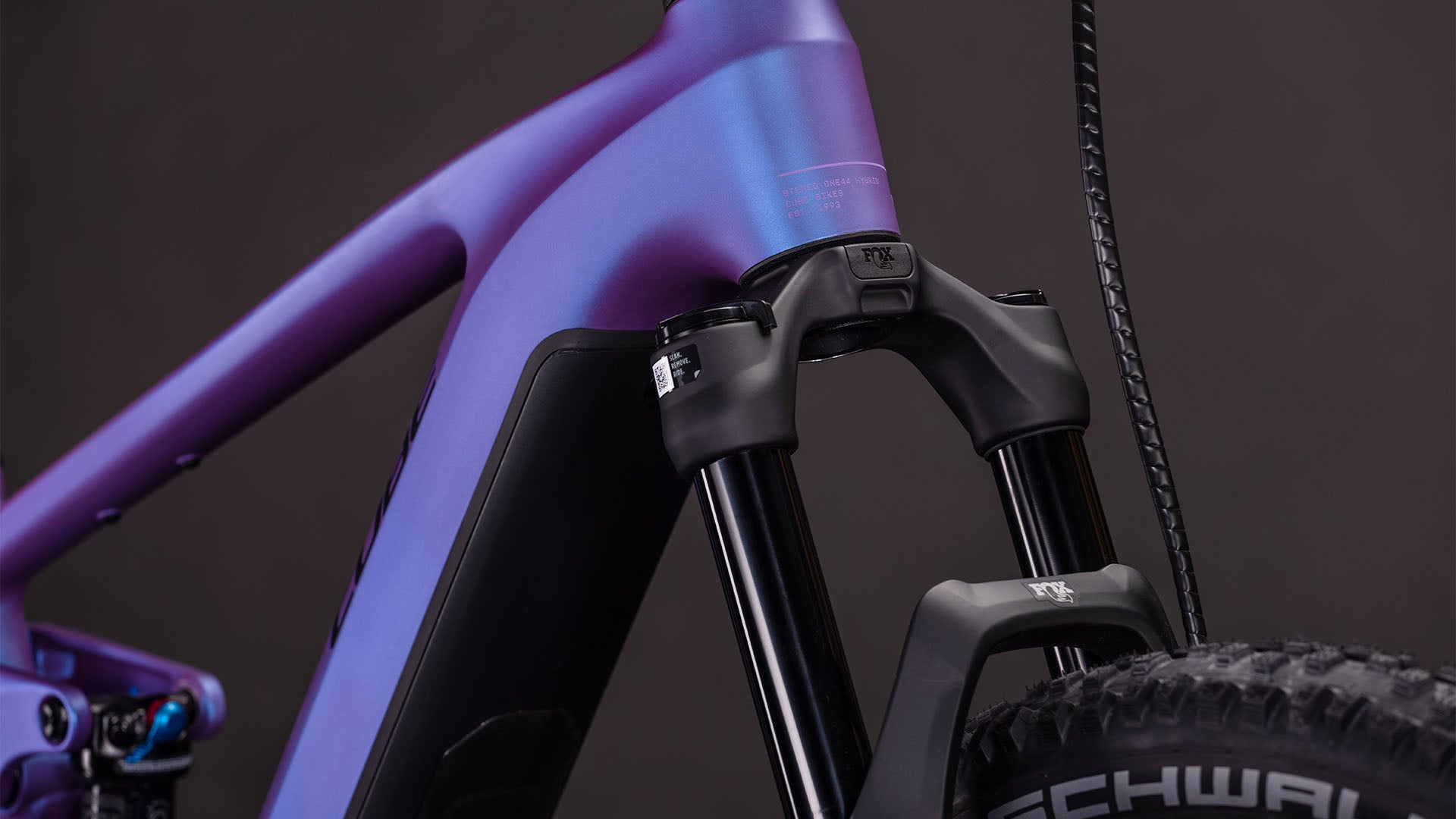 Nahaufnahme des CUBE Stereo Hybrid ONE44 EXC 800 blueiris'n'black 2026, die den lila und blauen Rahmen, den Bosch CX-Motor, die Federgabel und die Schwalbe-Reifen vor einem dunklen Hintergrund hervorhebt.