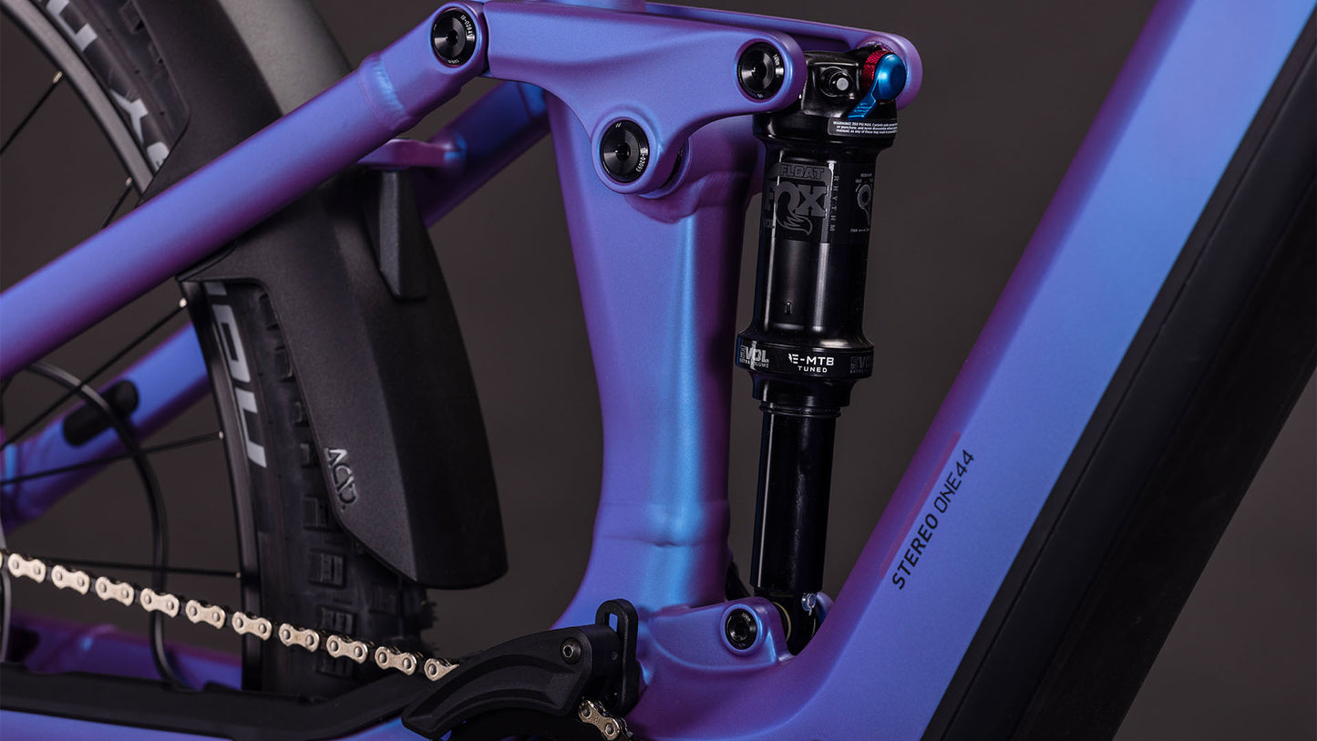 Nahaufnahme der Hinterradaufhängung, der Shimano XT Schaltung, des Stoßdämpfers, der Kette und der Reifen des CUBE Stereo Hybrid ONE44 EXC 800 blueiris'n'black 2026. Auf dem blau-schwarzen Rahmen steht "STEREO ONE44".