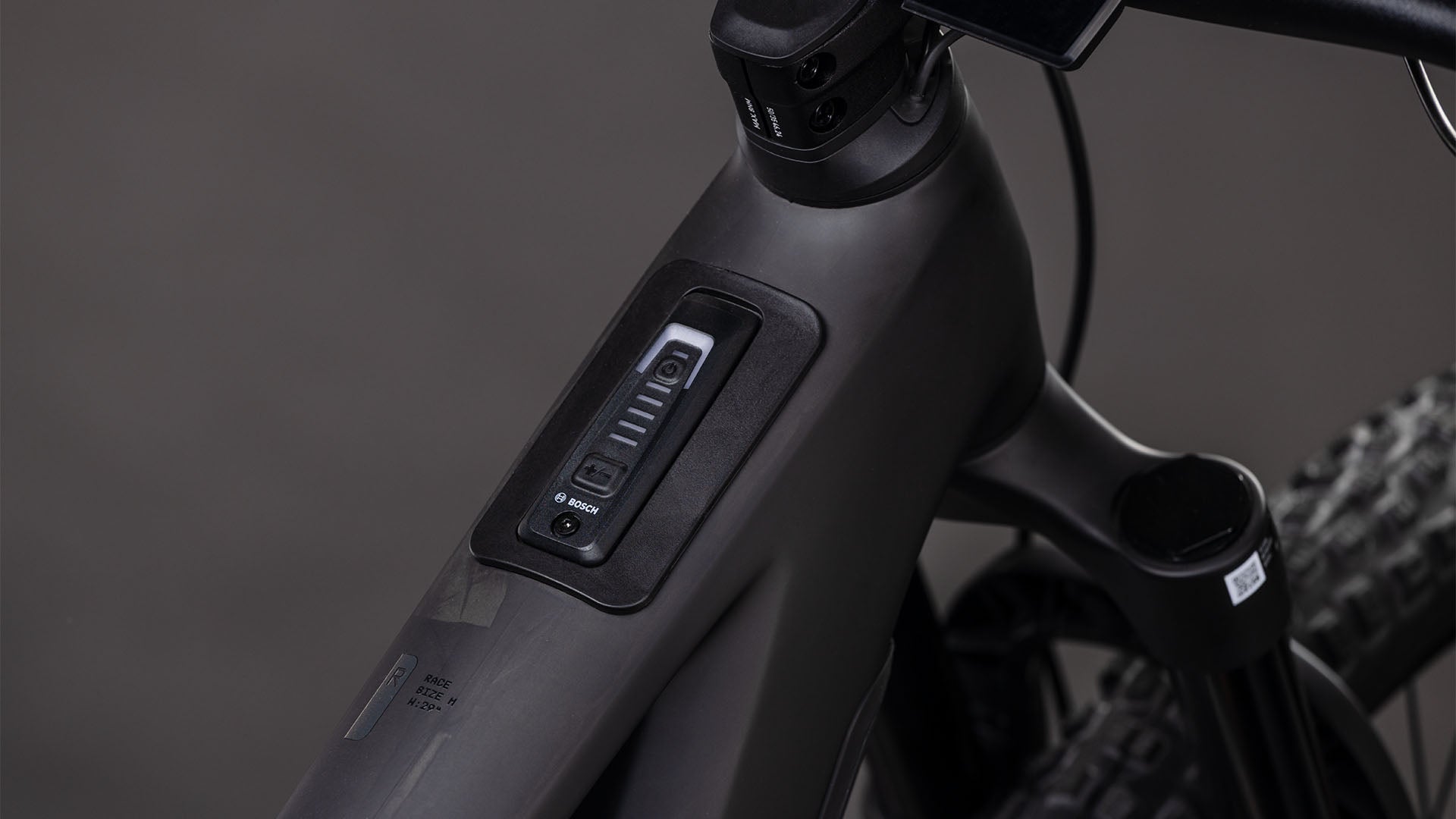 Nahaufnahme des Carbon-Rahmens des CUBE Stereo Hybrid ONE44 HPC Race 800 blackline 2026 mit dem eingebauten Bosch CX-Motor und dem Display in der Nähe des Lenkers sowie der vorderen Federung und den Reifen.