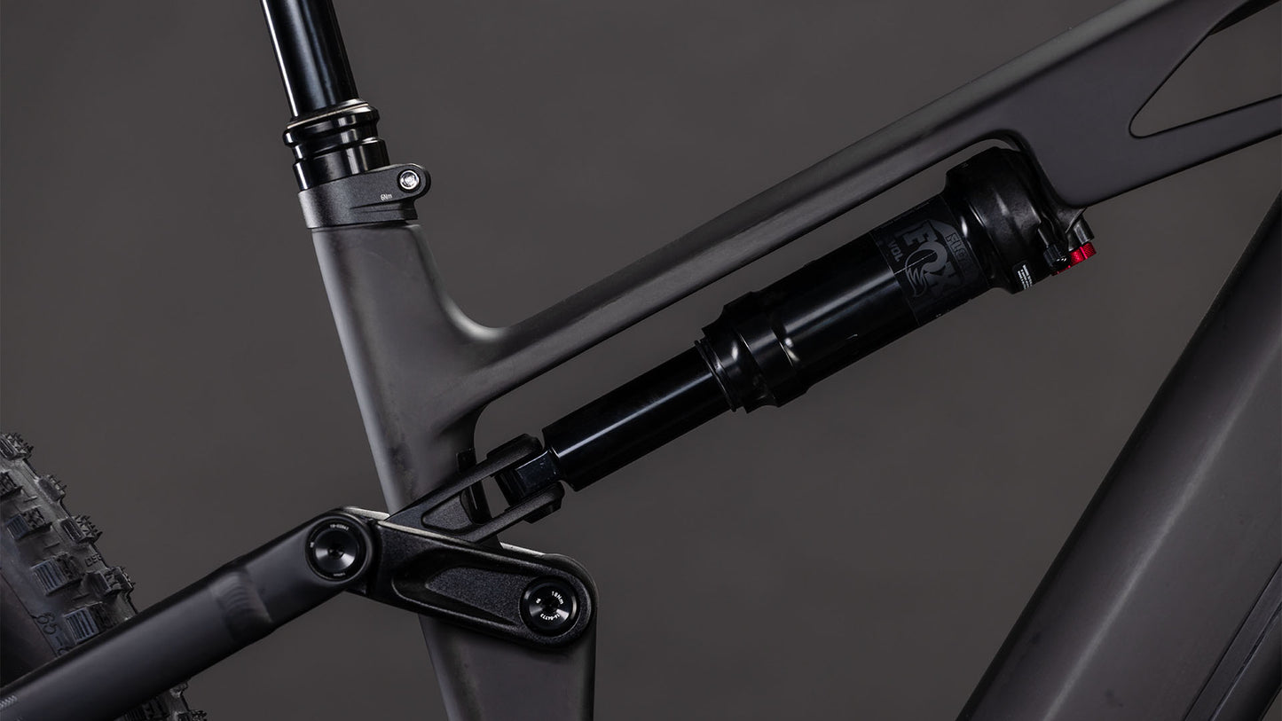 Nahaufnahme der Hinterradaufhängung des CUBE Stereo Hybrid ONE44 HPC Race 800 blackline 2026, die den Stoßdämpfer, das Gestänge und den Hochleistungs-Carbonrahmen vor einem dunklen Hintergrund hervorhebt.