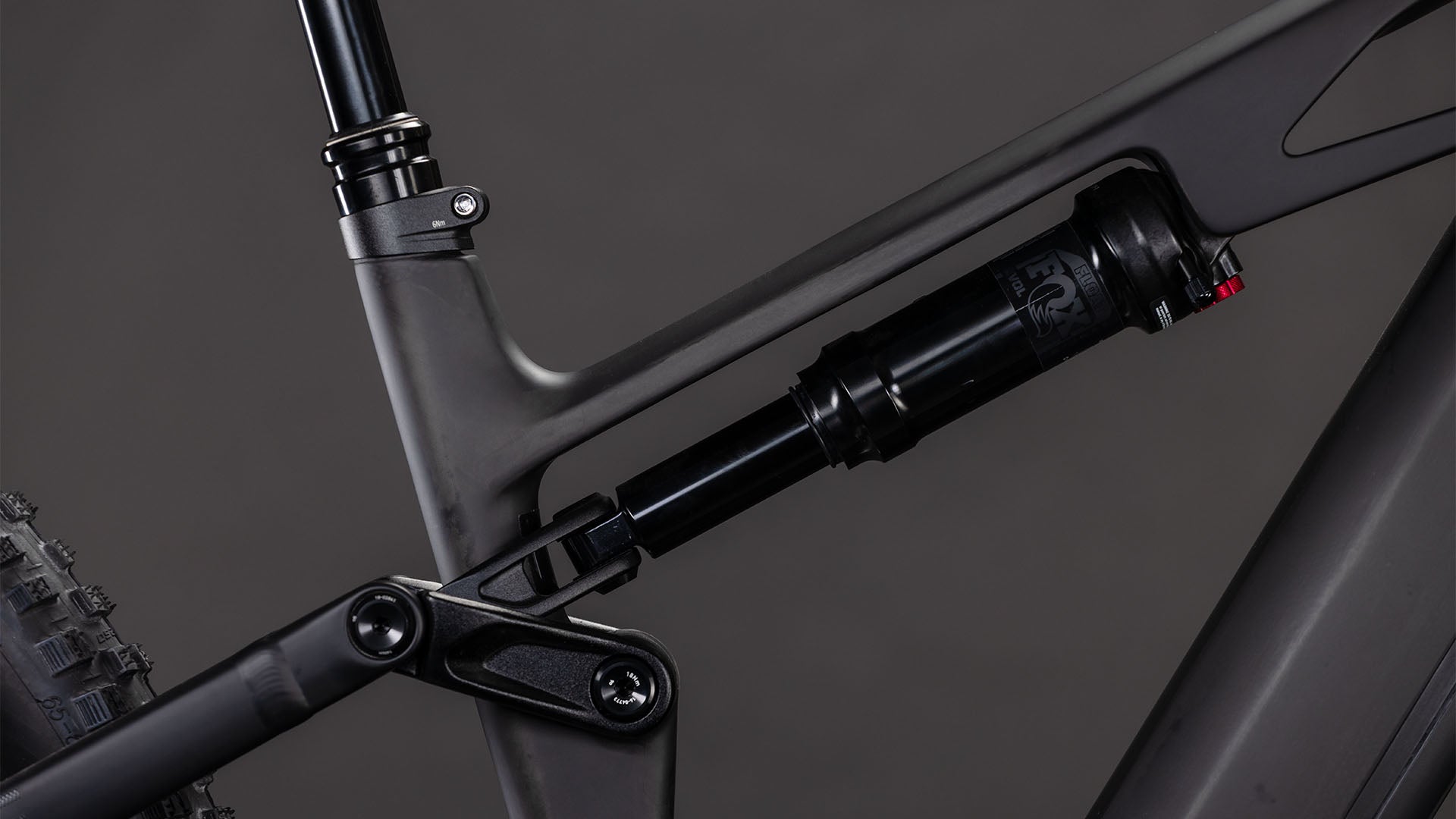 Nahaufnahme der Hinterradaufhängung des CUBE Stereo Hybrid ONE44 HPC Race 800 blackline 2026, die den Stoßdämpfer, das Gestänge und den Hochleistungs-Carbonrahmen vor einem dunklen Hintergrund hervorhebt.