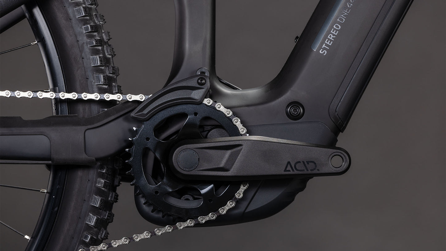 Nahaufnahme der CUBE Stereo Hybrid ONE44 HPC Race 800 blackline 2026 Kurbelgarnitur und Kette, mit schwarzen Pedalen, Kettenblatt, Carbonrahmen und dem nahtlos integrierten Bosch CX Motor. Einfarbig dunkelgrauer Hintergrund.