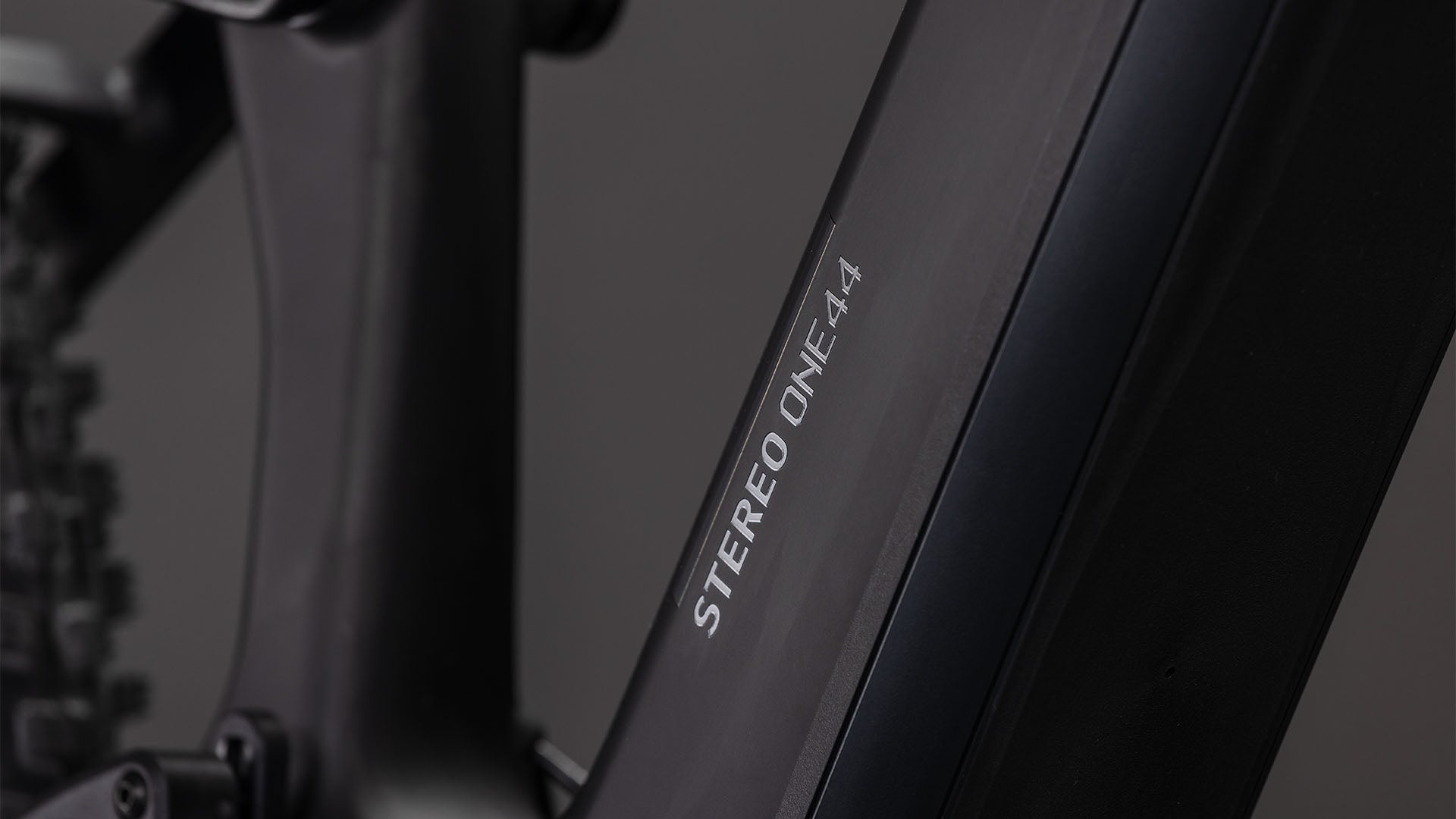 Nahaufnahme des mattschwarzen CUBE Stereo Hybrid ONE44 HPC Race 800 Fahrradrahmens mit dem vertikal in Weiß aufgedruckten ONE44 vor einem neutralgrauen Hintergrund.