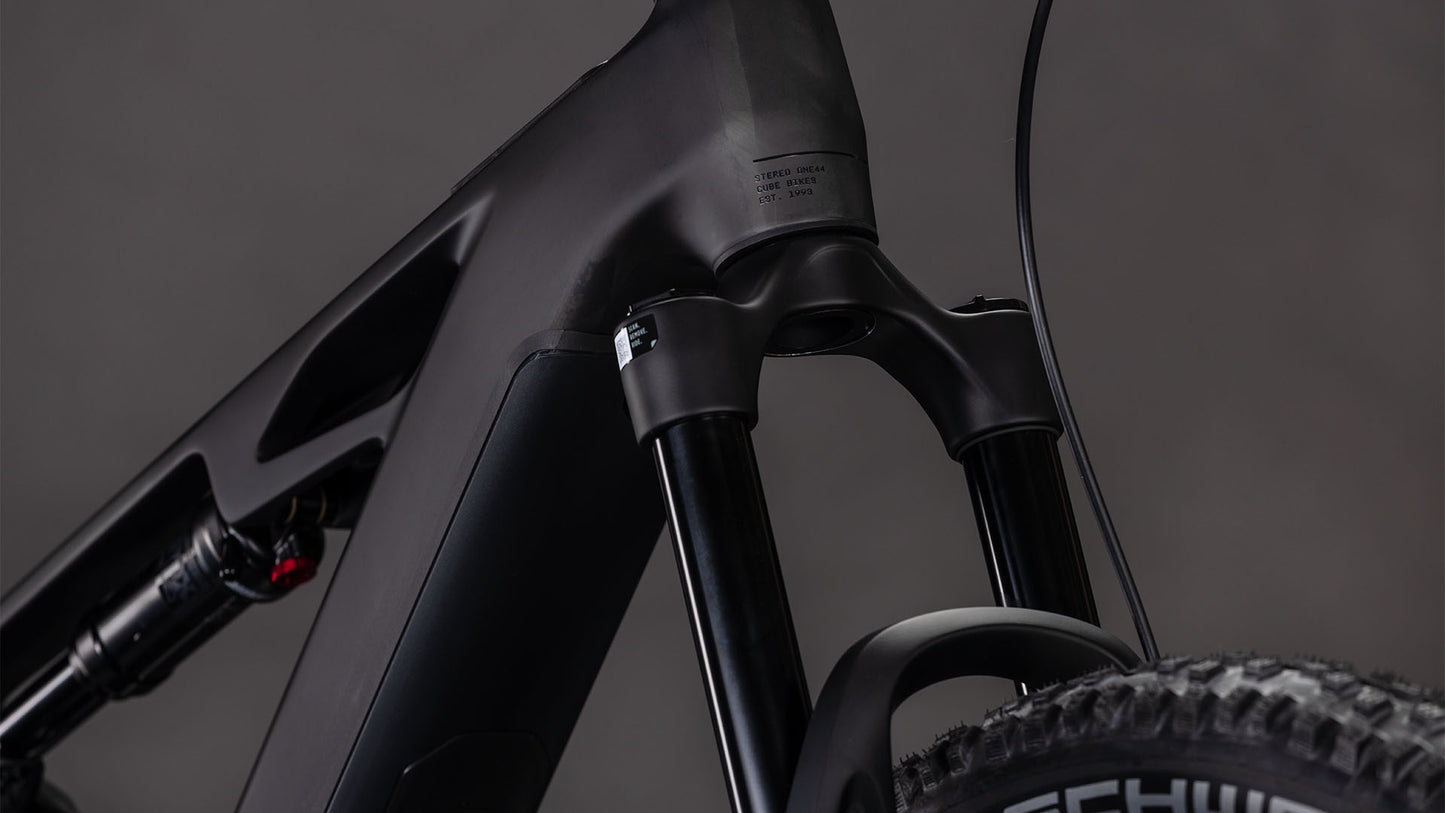 Nahaufnahme der CUBE Stereo Hybrid ONE44 HPC Race 800 blackline 2026 Federgabel, des High Performance Carbon Steuerrohrs, der Gabelstandrohre und eines Teils des Vorderradreifens vor einem neutralen Hintergrund.