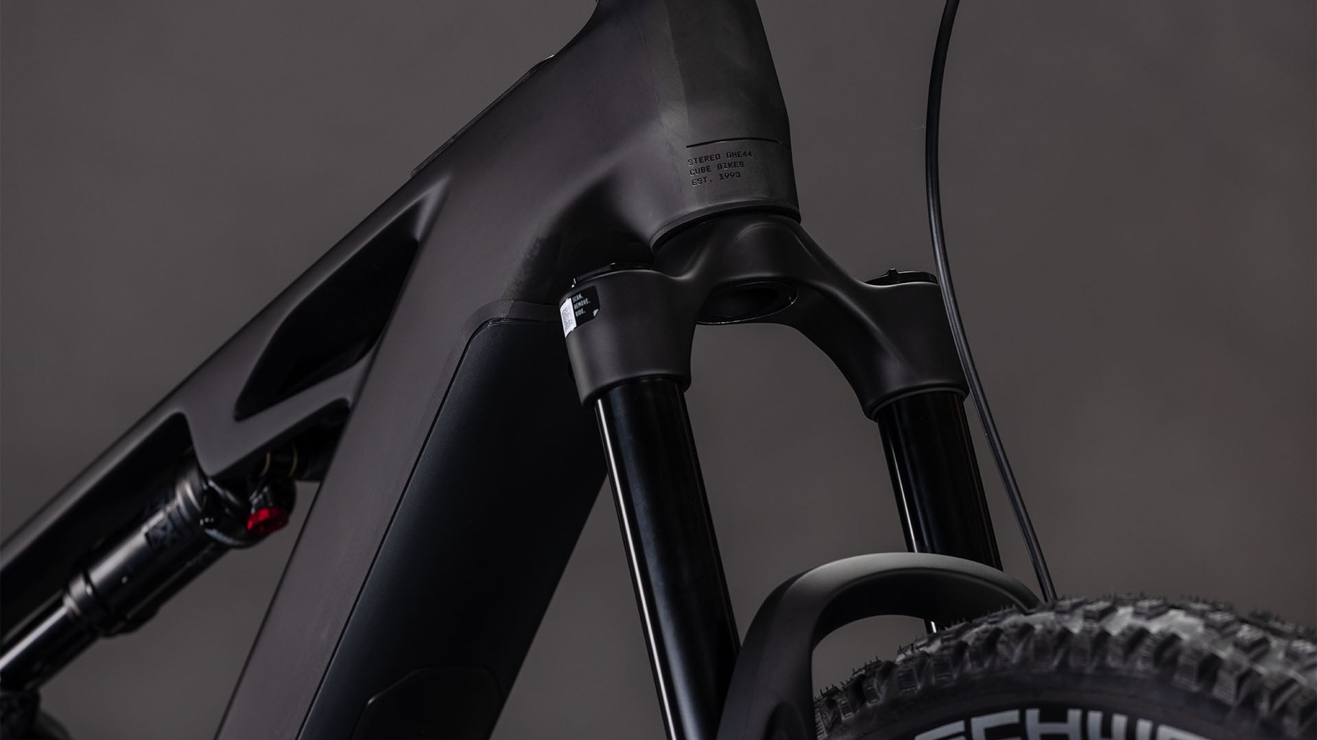 Nahaufnahme der CUBE Stereo Hybrid ONE44 HPC Race 800 blackline 2026 Federgabel, des High Performance Carbon Steuerrohrs, der Gabelstandrohre und eines Teils des Vorderradreifens vor einem neutralen Hintergrund.