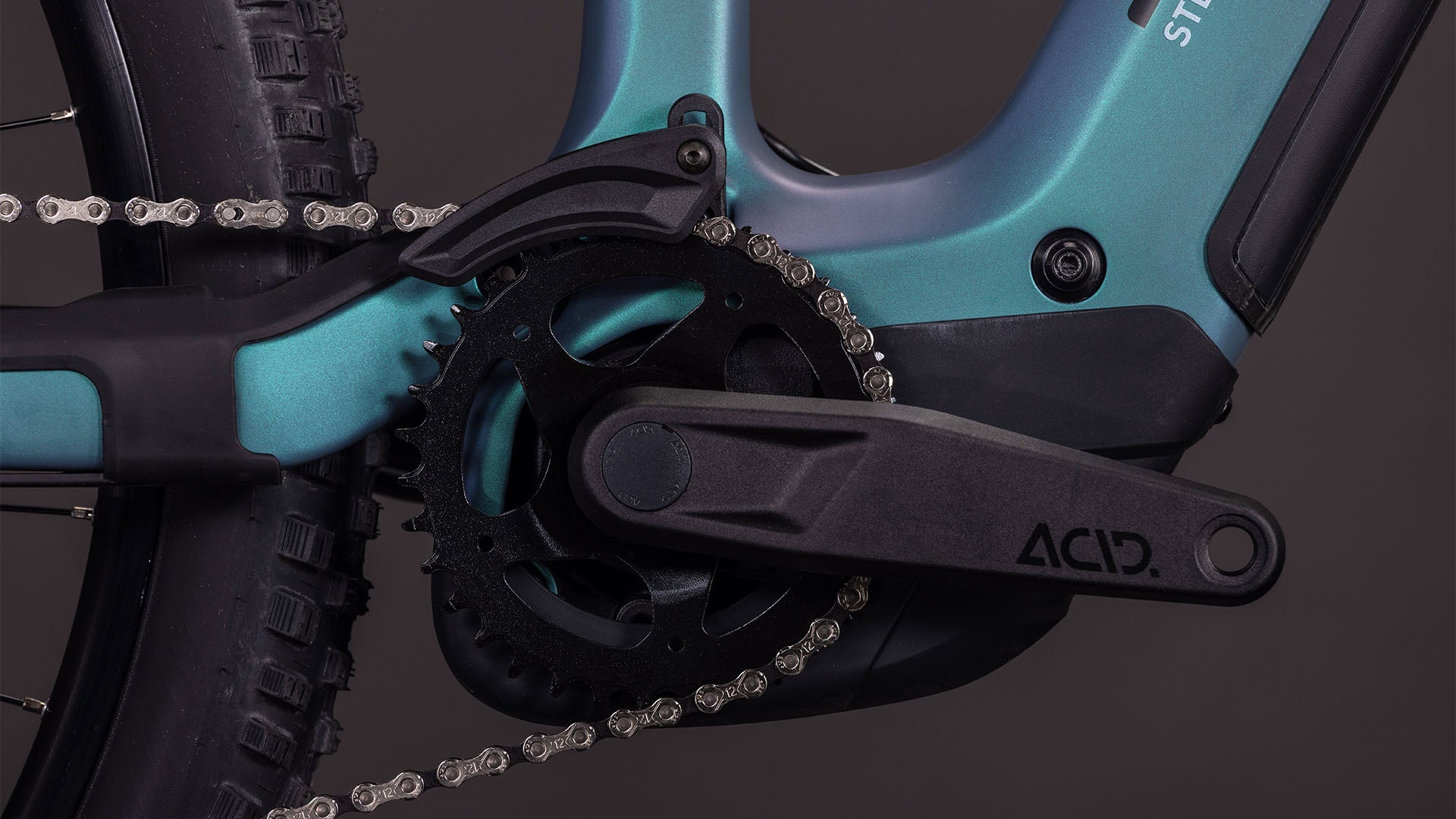 Nahaufnahme der CUBE Stereo Hybrid ONE44 HPC Race 800 smaragdgrey'n'prism 2026 Kurbelgarnitur mit schwarzem Kettenblatt, ACID-Pedalarm und silberner Kette, die leistungsstarke Carbon-Antriebskomponenten präsentiert.