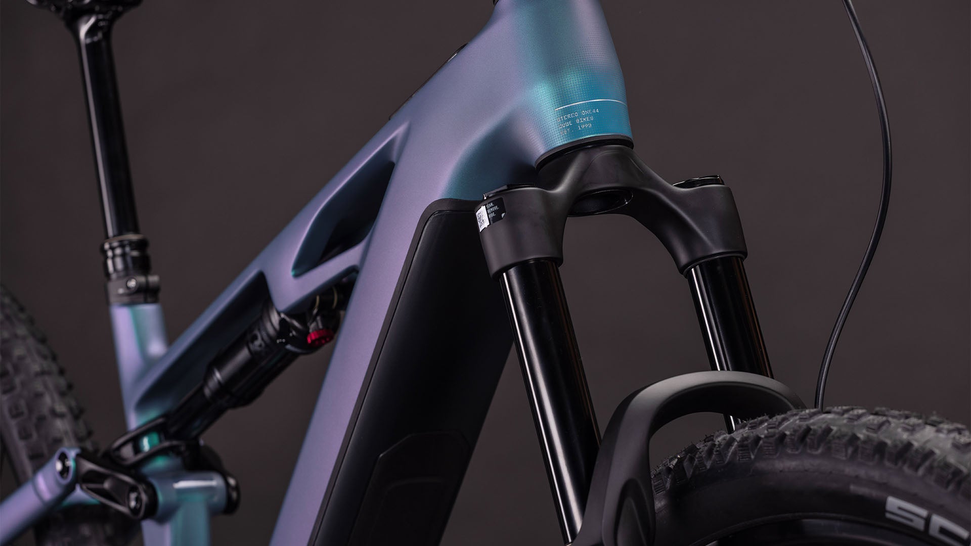 Nahaufnahme des CUBE Stereo Hybrid ONE44 HPC Race 800 (2026) in der Farbe smaragdgrey'n'prism, die den Carbonrahmen, die Federgabel, die dicken Reifen und die glatte, matte Oberfläche vor einem schwarzen Hintergrund zeigt.