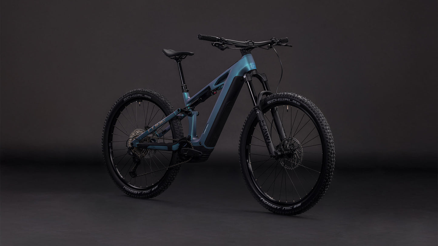 Das vollgefederte Mountainbike CUBE Stereo Hybrid ONE44 HPC Race 800 smaragdgrey'n'prism 2026 mit modernem Rahmen, schwarzen Komponenten und grobstolligen Reifen steht schräg vor einem dunklen Hintergrund.
