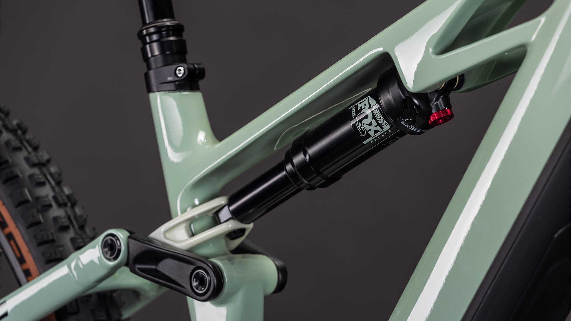 Nahaufnahme der Hinterradaufhängung des CUBE Stereo Hybrid ONE44 HPC Race 800, die den Stoßdämpfer und den hellgrünen (driedherbs'n'black) Hochleistungs-Carbonrahmen vor einem dunklen Hintergrund zeigt.