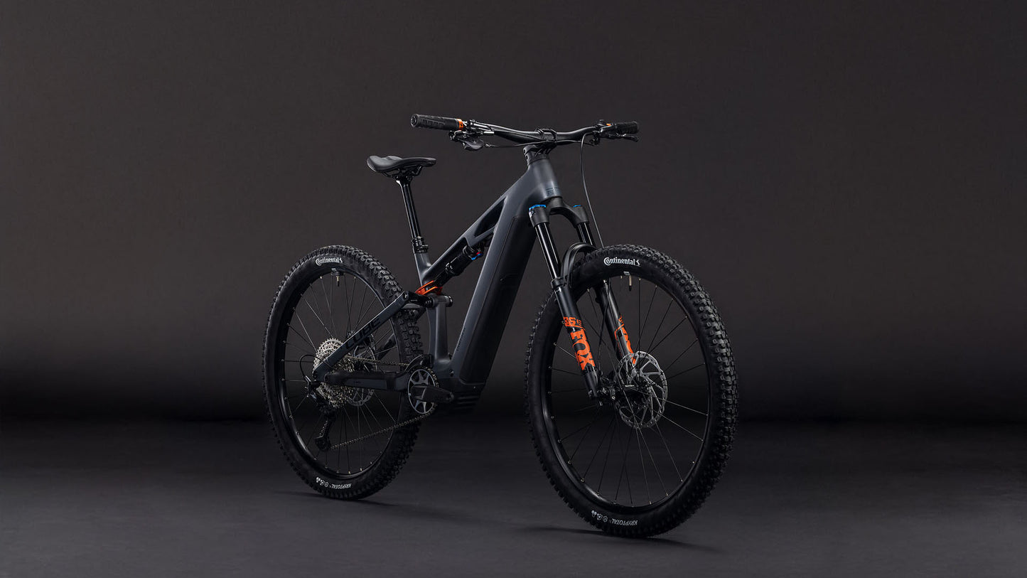 Das CUBE Stereo Hybrid ONE44 HPC SLX 800 slabgrey'n'orange 2026 Mountainbike mit Bosch CX Motor, Shimano XT Schaltung, Scheibenbremsen und orangen Akzenten steht aufrecht und schräg links vor einem dunklen Hintergrund.