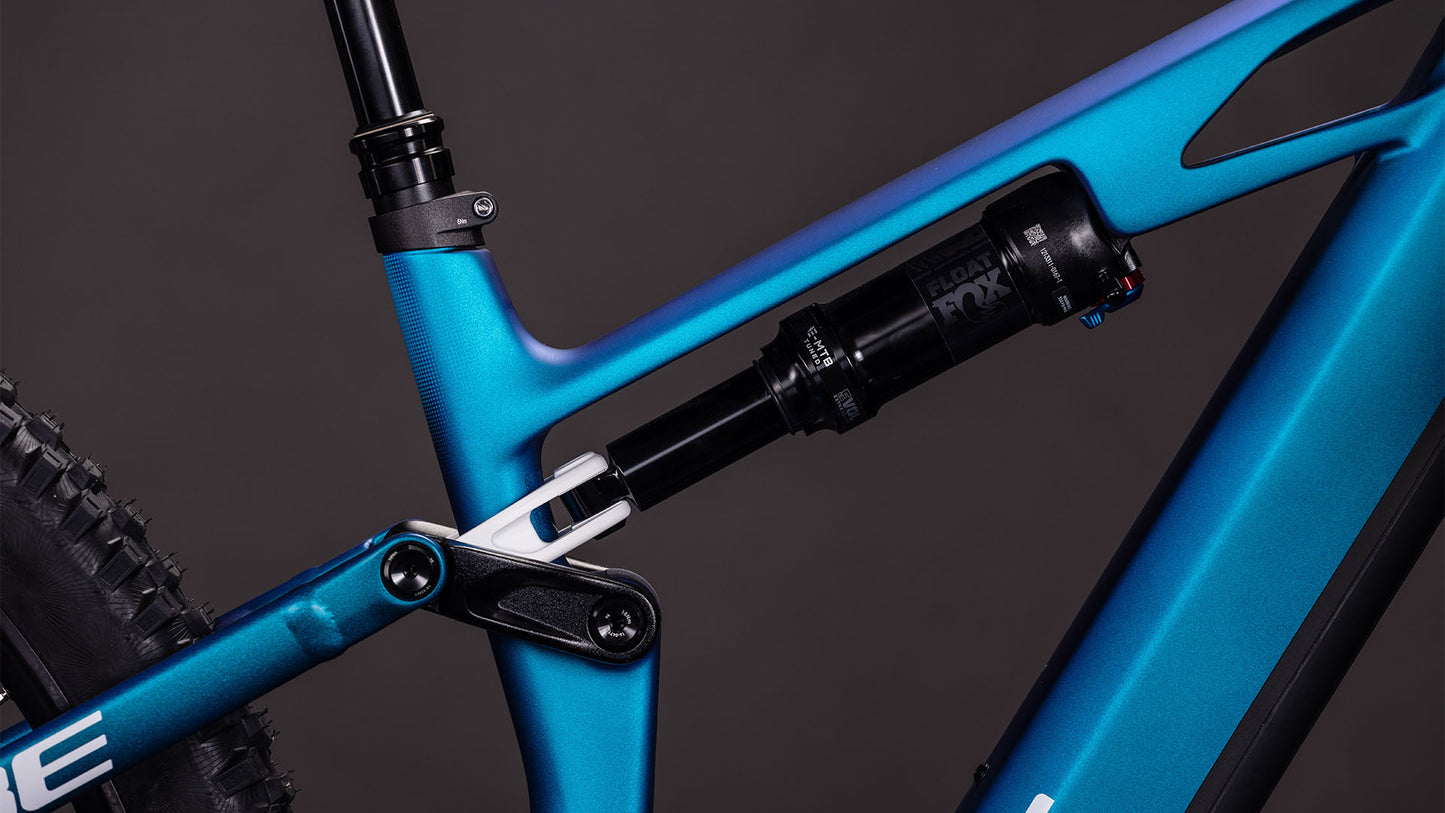 Nahaufnahme des CUBE Stereo Hybrid ONE44 HPC SLX 800 nebula'n'white 2026 Mountainbike-Rahmens, die die hintere Federung, das Gestänge, die Shimano XT 12-fach Schaltung und das Hinterrad vor einem dunklen Hintergrund zeigt.