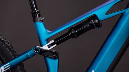 Nahaufnahme des CUBE Stereo Hybrid ONE44 HPC SLX 800 nebula'n'white 2026 Mountainbike-Rahmens, die die hintere Federung, das Gestänge, die Shimano XT 12-fach Schaltung und das Hinterrad vor einem dunklen Hintergrund zeigt.