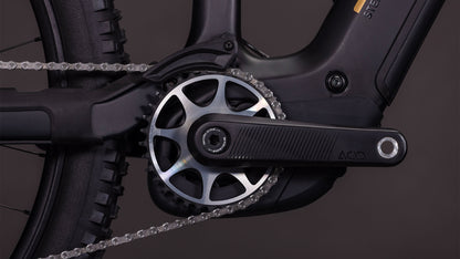Nahaufnahme des Cube Stereo Hybrid ONE44 HPC AT 800 carbon'n'gold 2026 von CUBE, die die Kurbelgarnitur, das Kettenblatt, die Kette und den Pedalarm in der Nähe des Hinterrads vor einem dunklen Hintergrund zeigt - mit dem fortschrittlichen Bosch CX Motor für nahtlose Leistung.