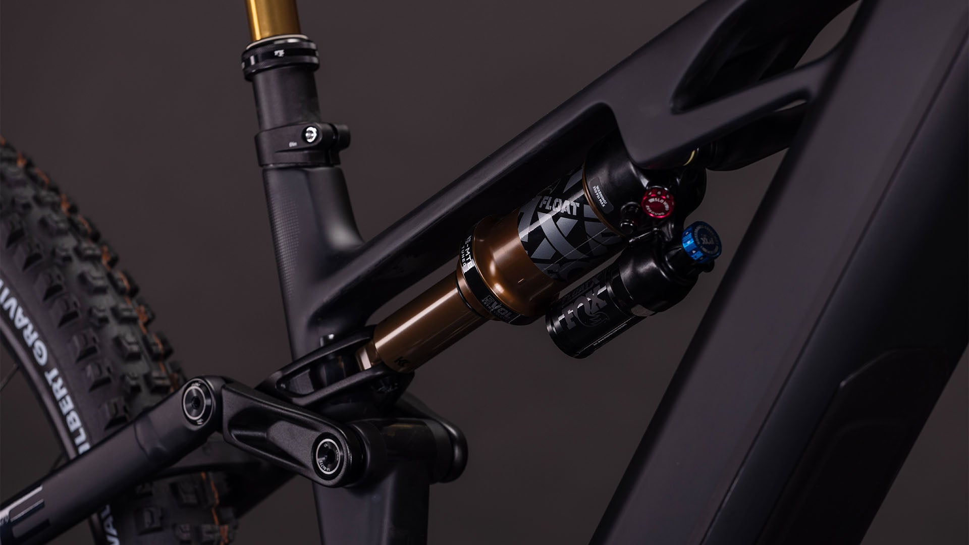 Nahaufnahme der Hinterradfederung des CUBE Stereo Hybrid ONE44 HPC AT 800 carbon'n'gold 2026 mit einem FOX FLOAT X-Dämpfer auf einem mattschwarzen Rahmen. Shimano XT-Komponenten steigern die Leistung, ein Teil des Hinterreifens und des Sitzrohrs sind sichtbar.