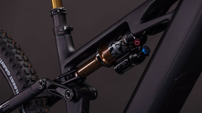 Nahaufnahme der Hinterradfederung des CUBE Stereo Hybrid ONE44 HPC AT 800 carbon'n'gold 2026 mit einem FOX FLOAT X-Dämpfer auf einem mattschwarzen Rahmen. Shimano XT-Komponenten steigern die Leistung, ein Teil des Hinterreifens und des Sitzrohrs sind sichtbar.