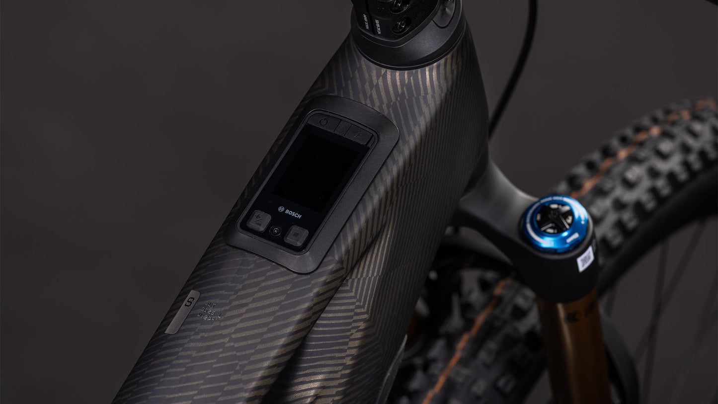 Nahaufnahme des CUBE Stereo Hybrid ONE44 HPC SLT 800 (carbongrid'n'chrome, 2026): zeigt das strukturierte Carbon-Oberrohr mit Digitalanzeige und Bedienelementen. Der Bosch CX-R-Motor, der 800-Wh-Akku, die Vorderradaufhängung und die Reifen unterstreichen seine All-Mountain-E-Bike-Power.