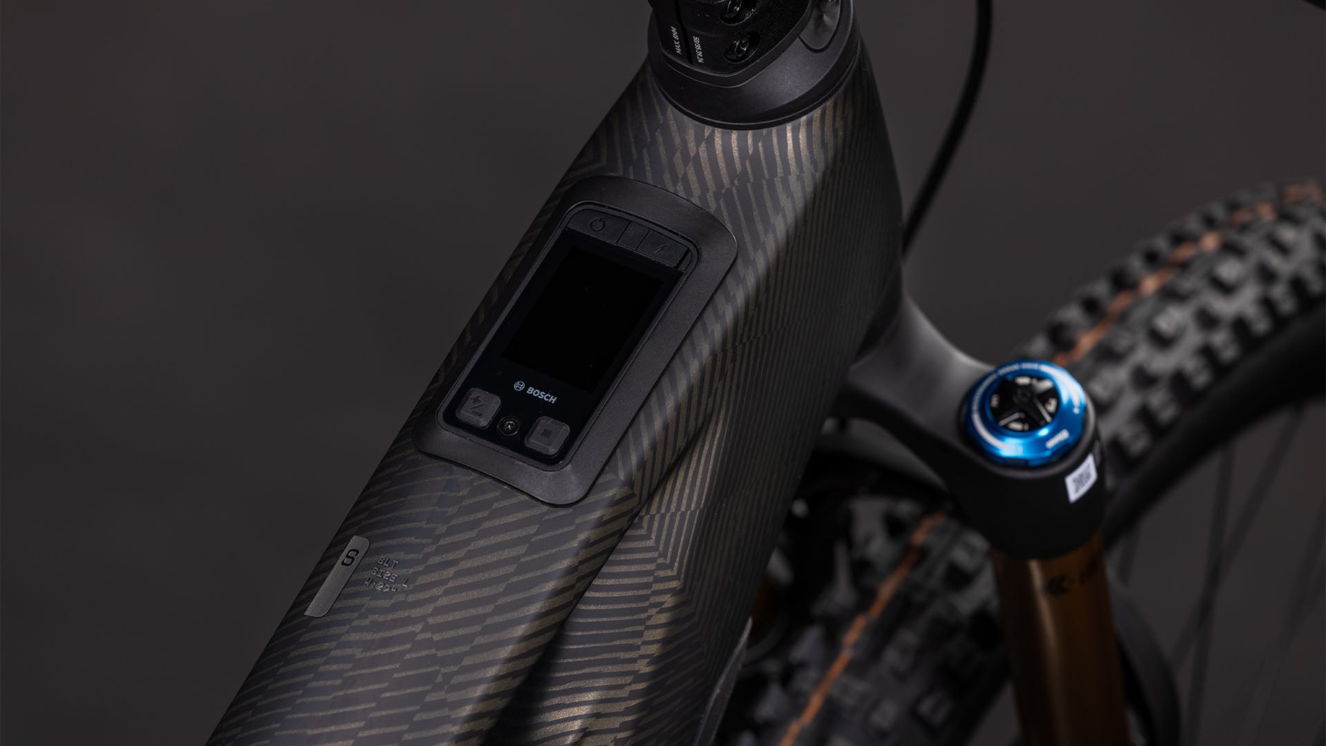 Nahaufnahme des CUBE Stereo Hybrid ONE44 HPC SLT 800 (carbongrid'n'chrome, 2026): zeigt das strukturierte Carbon-Oberrohr mit Digitalanzeige und Bedienelementen. Der Bosch CX-R-Motor, der 800-Wh-Akku, die Vorderradaufhängung und die Reifen unterstreichen seine All-Mountain-E-Bike-Power.