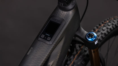 Nahaufnahme des CUBE Stereo Hybrid ONE44 HPC SLT 800 (carbongrid'n'chrome, 2026): zeigt das strukturierte Carbon-Oberrohr mit Digitalanzeige und Bedienelementen. Der Bosch CX-R-Motor, der 800-Wh-Akku, die Vorderradaufhängung und die Reifen unterstreichen seine All-Mountain-E-Bike-Power.