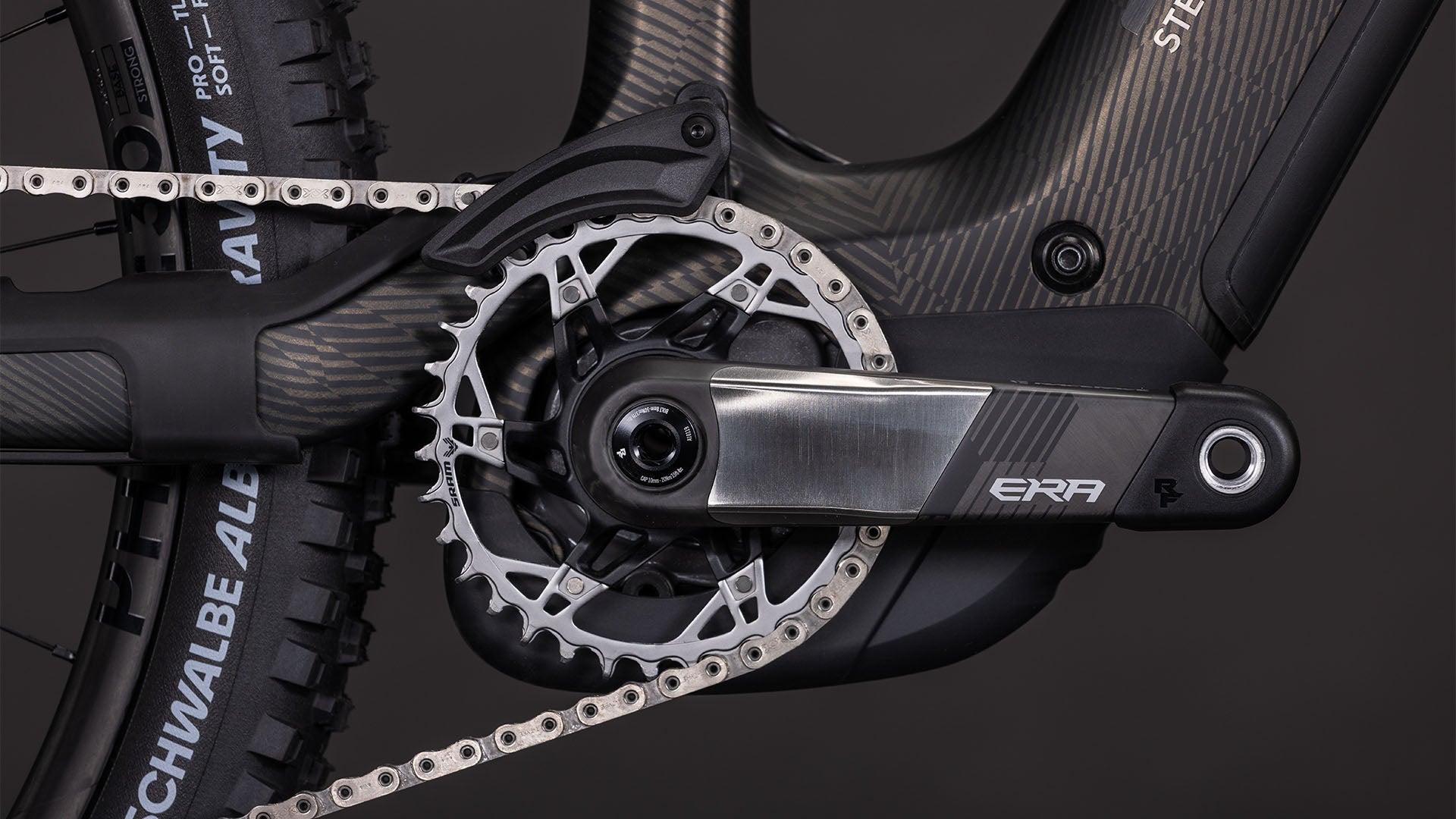 Nahaufnahme der CUBE Stereo Hybrid ONE44 HPC SLT 800 Kurbelgarnitur und des Kettenblatts mit Metallic-Finish, ERA-Logo, All-Mountain-E-Bike-Rahmen, Hinterradreifen, einem Teil der Kette und einem Bosch CX-R Motor. Marke: CUBE.