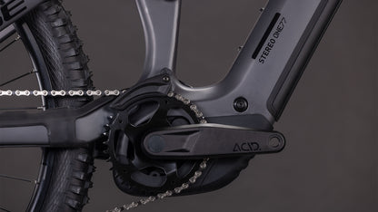 Nahaufnahme einer schwarzen Kurbelgarnitur, Kette und Rahmen des CUBE Stereo Hybrid ONE77 HPC Race 800 irongrey'n'black 2026, mit sichtbarer STEREO ONE77. Der dunkle Hintergrund hebt das Design und die Details der Shimano XT 12-fach Schaltung hervor.