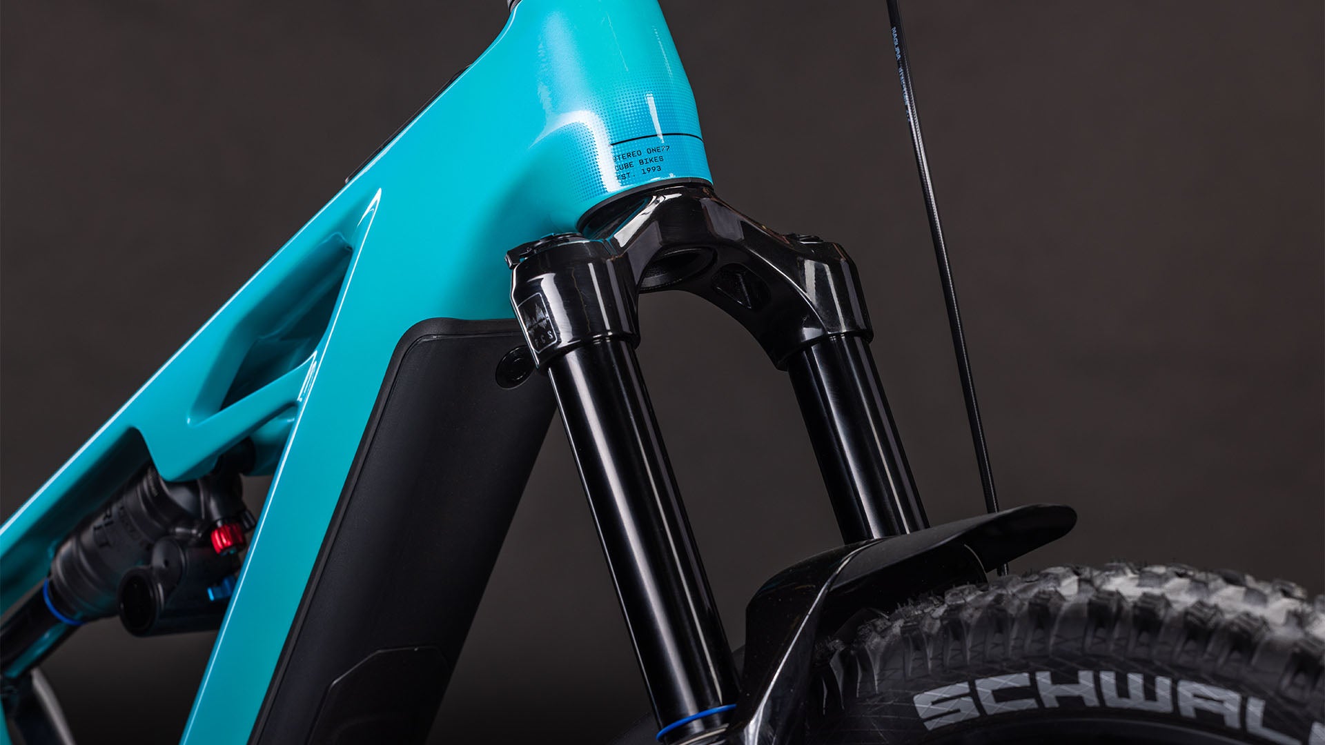 Nahaufnahme der vorderen Federgabel, des Stoßdämpfers und des Schwalbe-Reifenprofils am CUBE Stereo Hybrid ONE77 HPC Race 800 swimmingpool'n'black 2026 Mountainbike, wobei der Rahmen vor einem dunklen Hintergrund hervorgehoben wird.