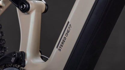 Nahaufnahme des CUBE Stereo Hybrid ONE77 HPC SLX 800 glintsand'n'black 2026 Rahmens, die einen Teil der Hinterradaufhängung, Fahrradkomponenten und den beeindruckenden Federweg von 170 mm zeigt, mit STEREO ONE77 Branding vor dunklem Hintergrund.