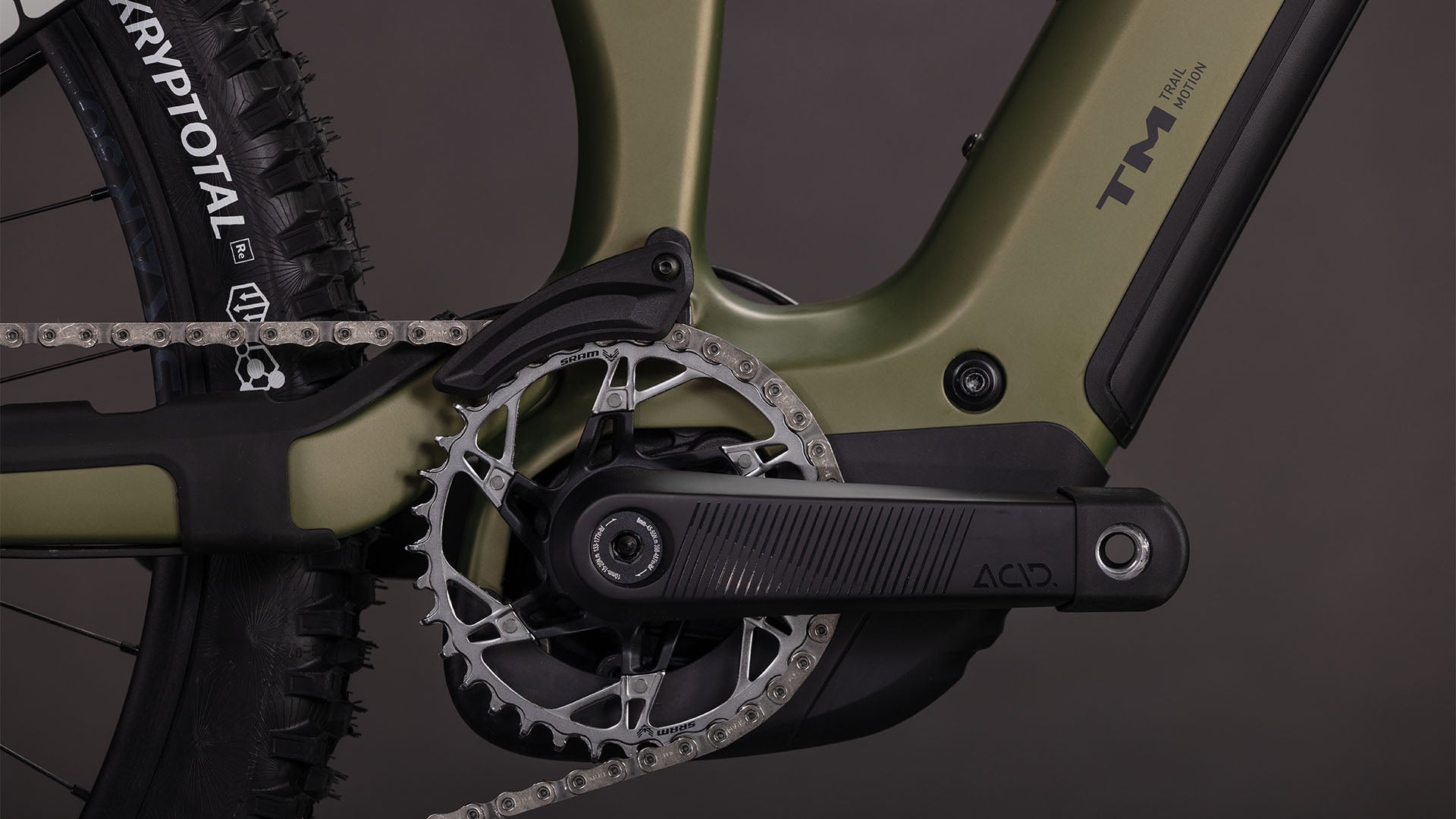 Nahaufnahme des Cube Stereo Hybrid ONE77 HPC TM 800 reedgreen'n'matrix 2026 von CUBE. Hervorzuheben sind die Kurbelgarnitur, das Kettenblatt, die Kette, der Pedalarm, der KRYPTOTAL-Hinterreifen, der schilfgrüne Rahmen mit schwarzen Akzenten und der leistungsstarke Bosch CX-Motor.